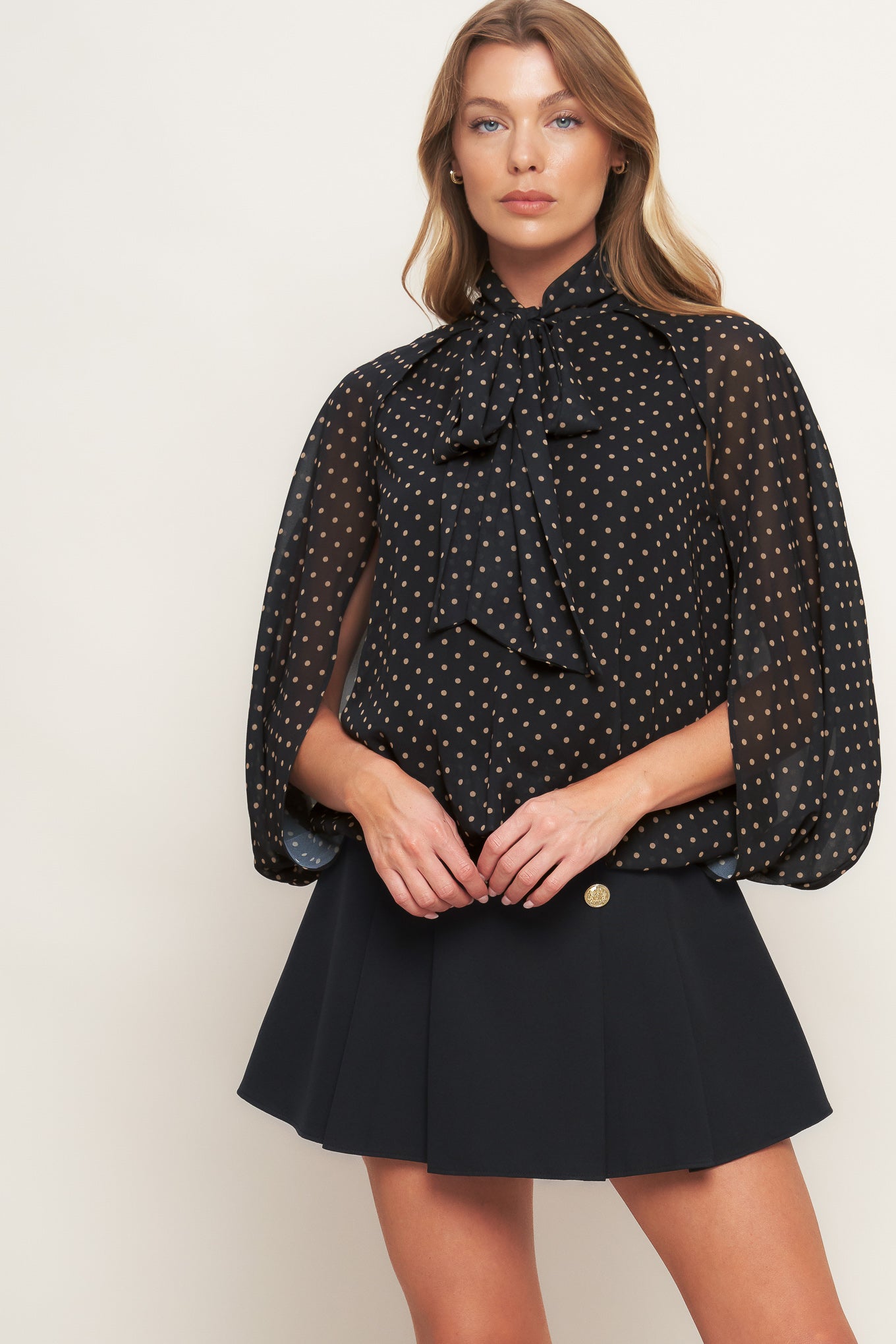 A woven dotted top featuring front bow tie and capelet.