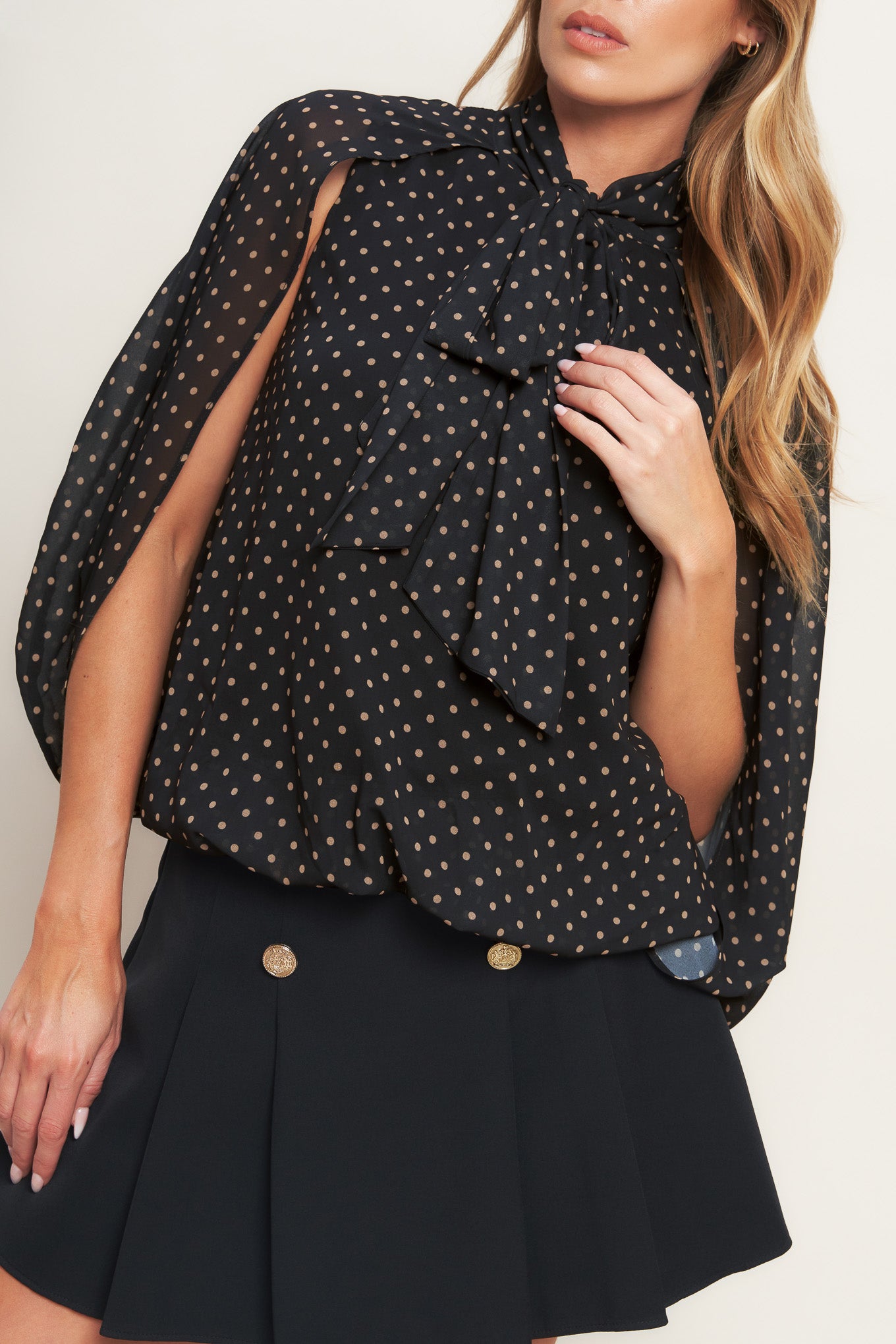 A woven dotted top featuring front bow tie and capelet.