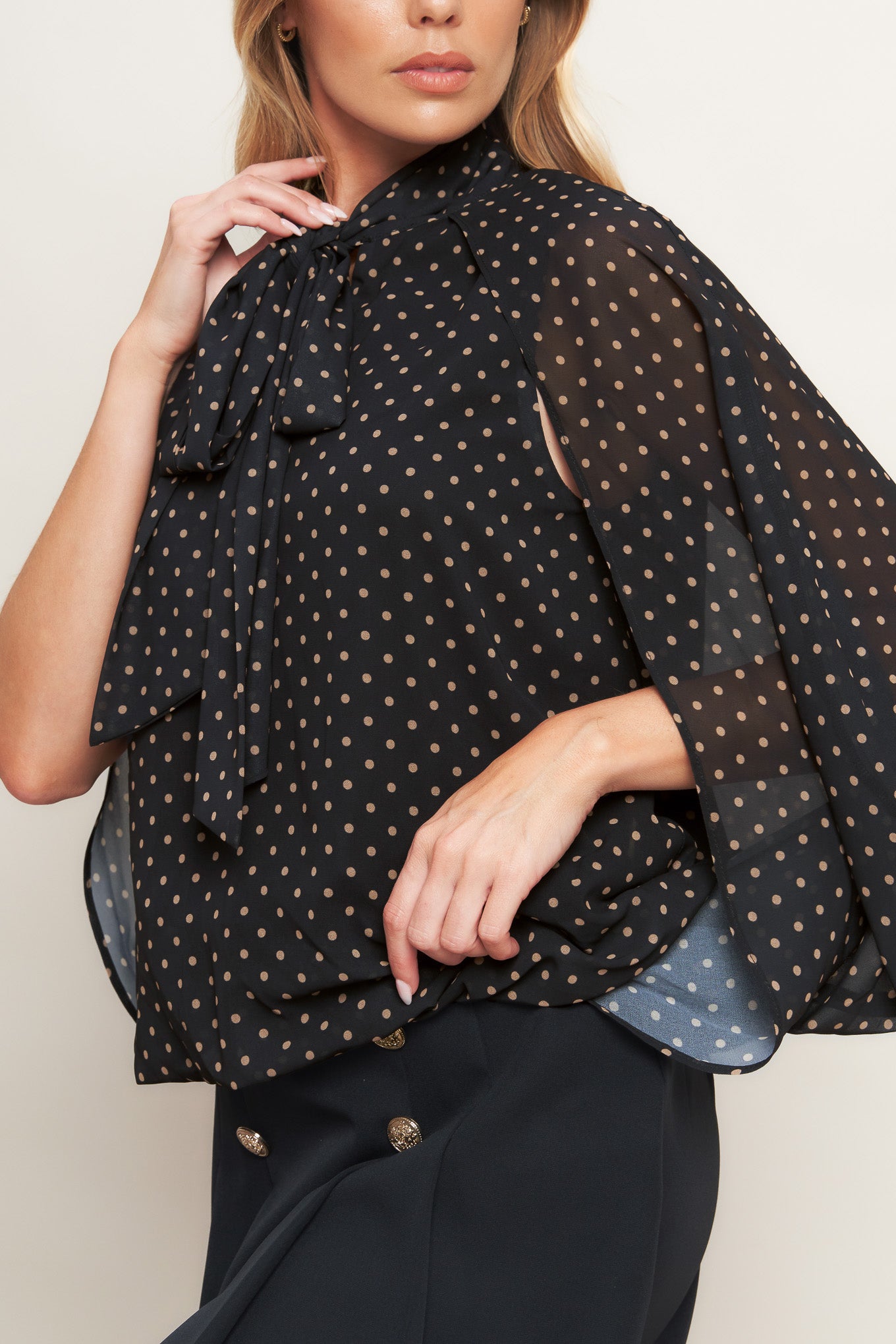 A woven dotted top featuring front bow tie and capelet.