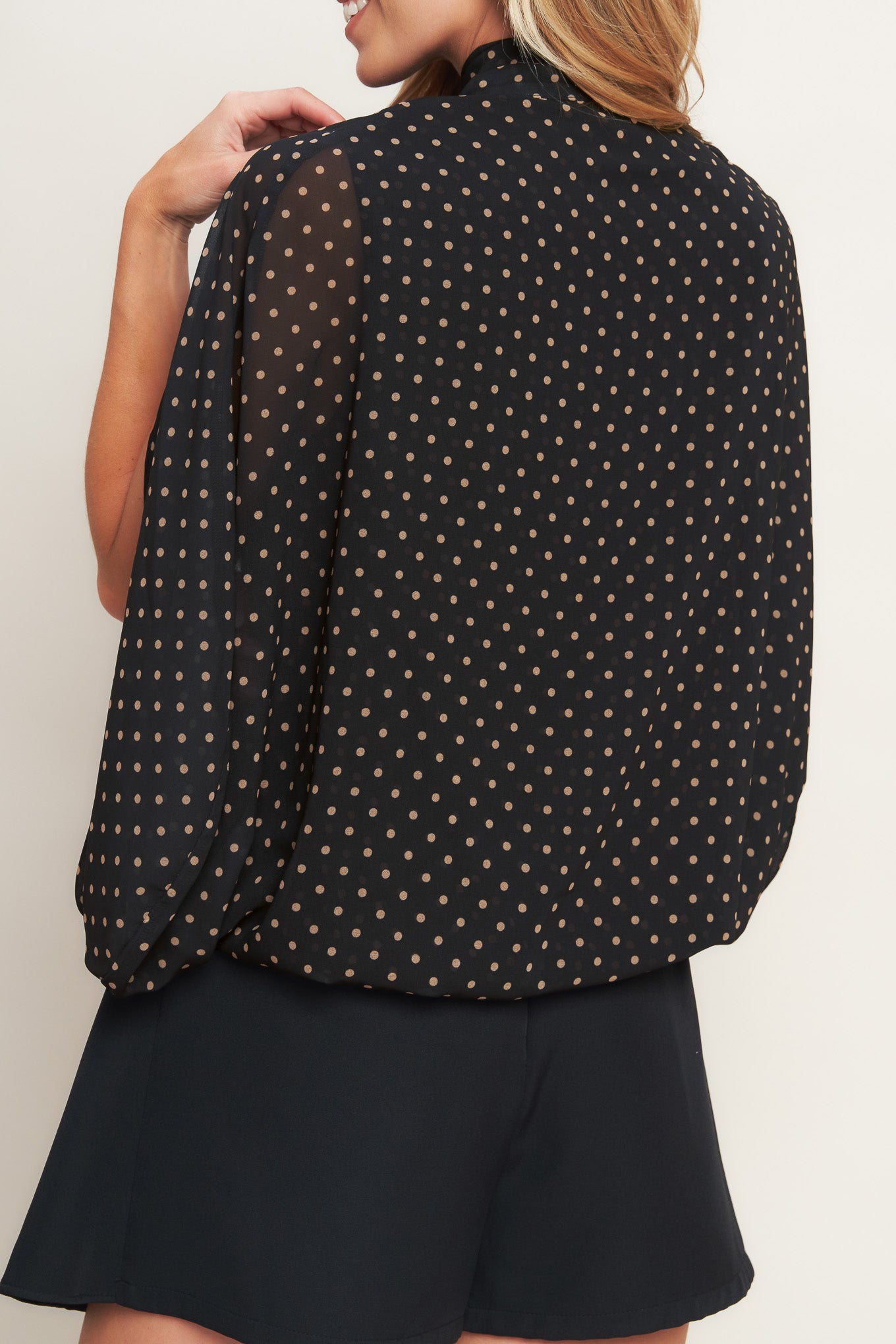 A woven dotted top featuring front bow tie and capelet.