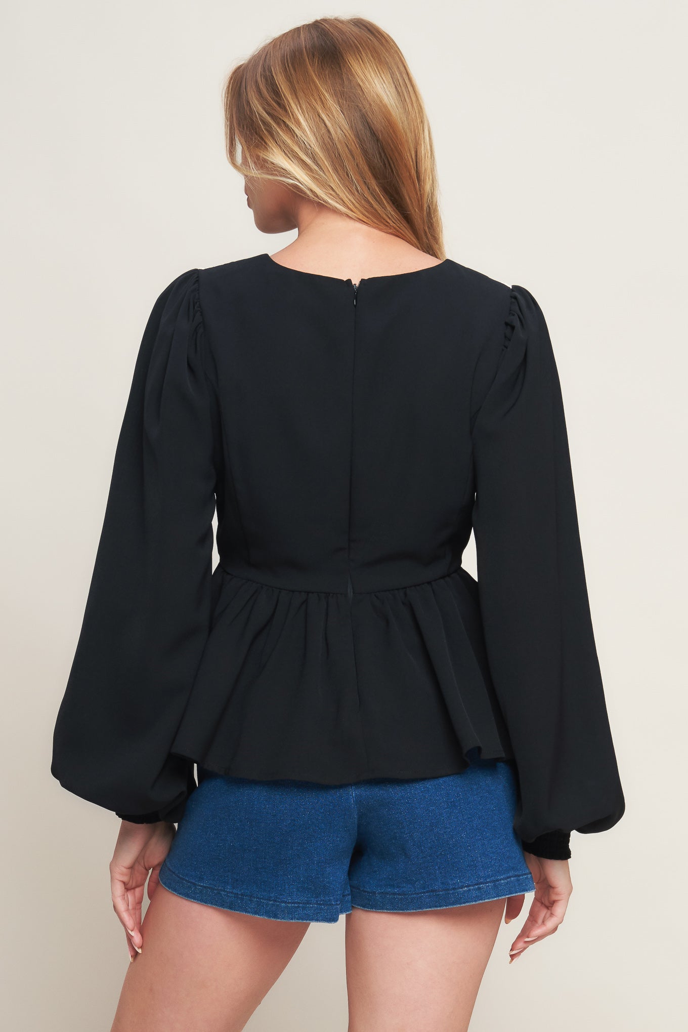 A solid woven top featuring round neckline, long sleeve, embellished bodice, peplum and back zipper closure