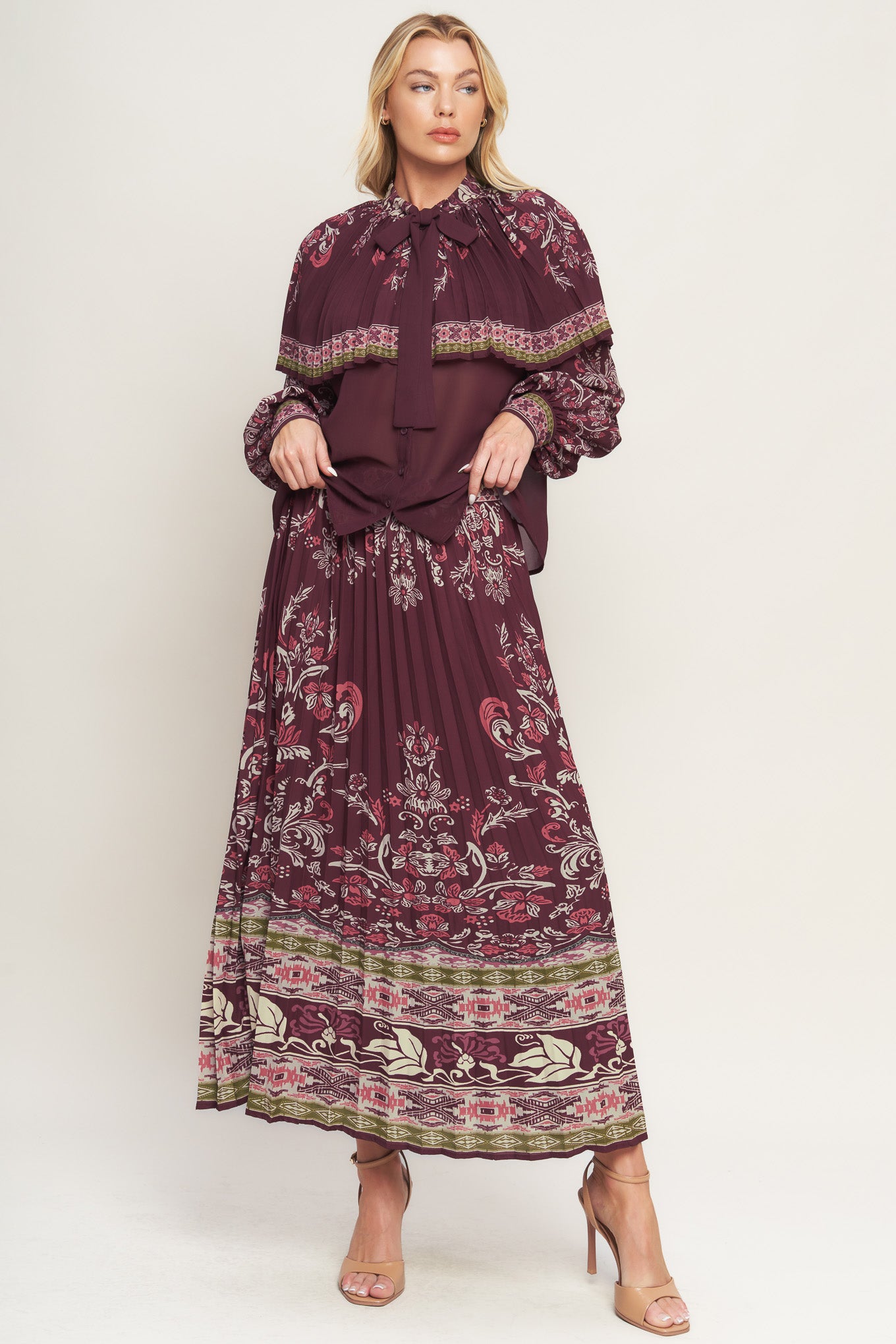 A printed woven top featuring pleated capelet, front bow tie, button down and long sleeve with cuff. 