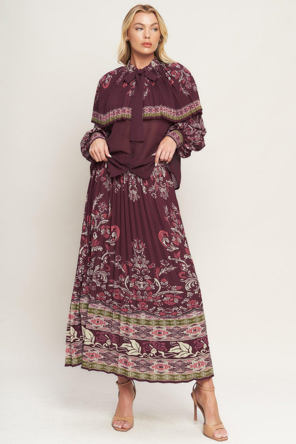 A printed woven top featuring pleated capelet, front bow tie, button down and long sleeve with cuff. 