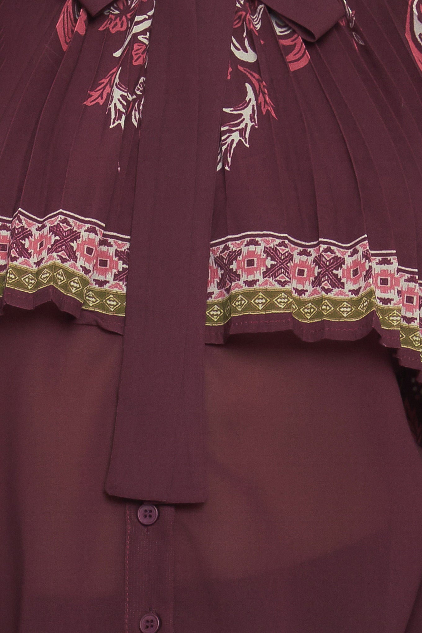 A printed woven top featuring pleated capelet, front bow tie, button down and long sleeve with cuff. 