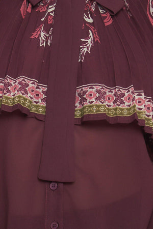 A printed woven top featuring pleated capelet, front bow tie, button down and long sleeve with cuff. 