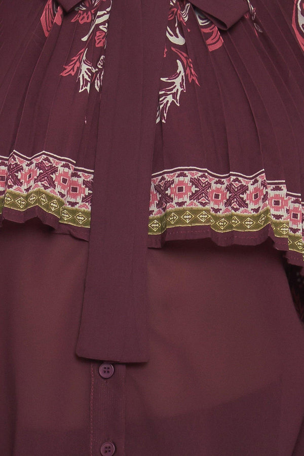 A printed woven top featuring pleated capelet, front bow tie, button down and long sleeve with cuff. 