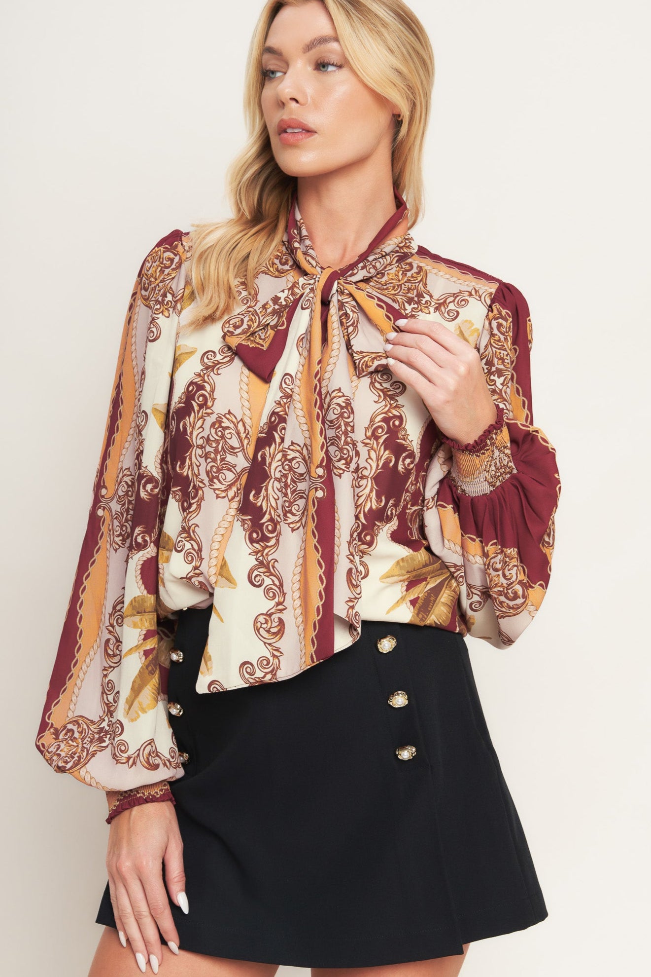 A printed woven top featuring front bow tie, long sleeve with smocked cuff and front button down closure