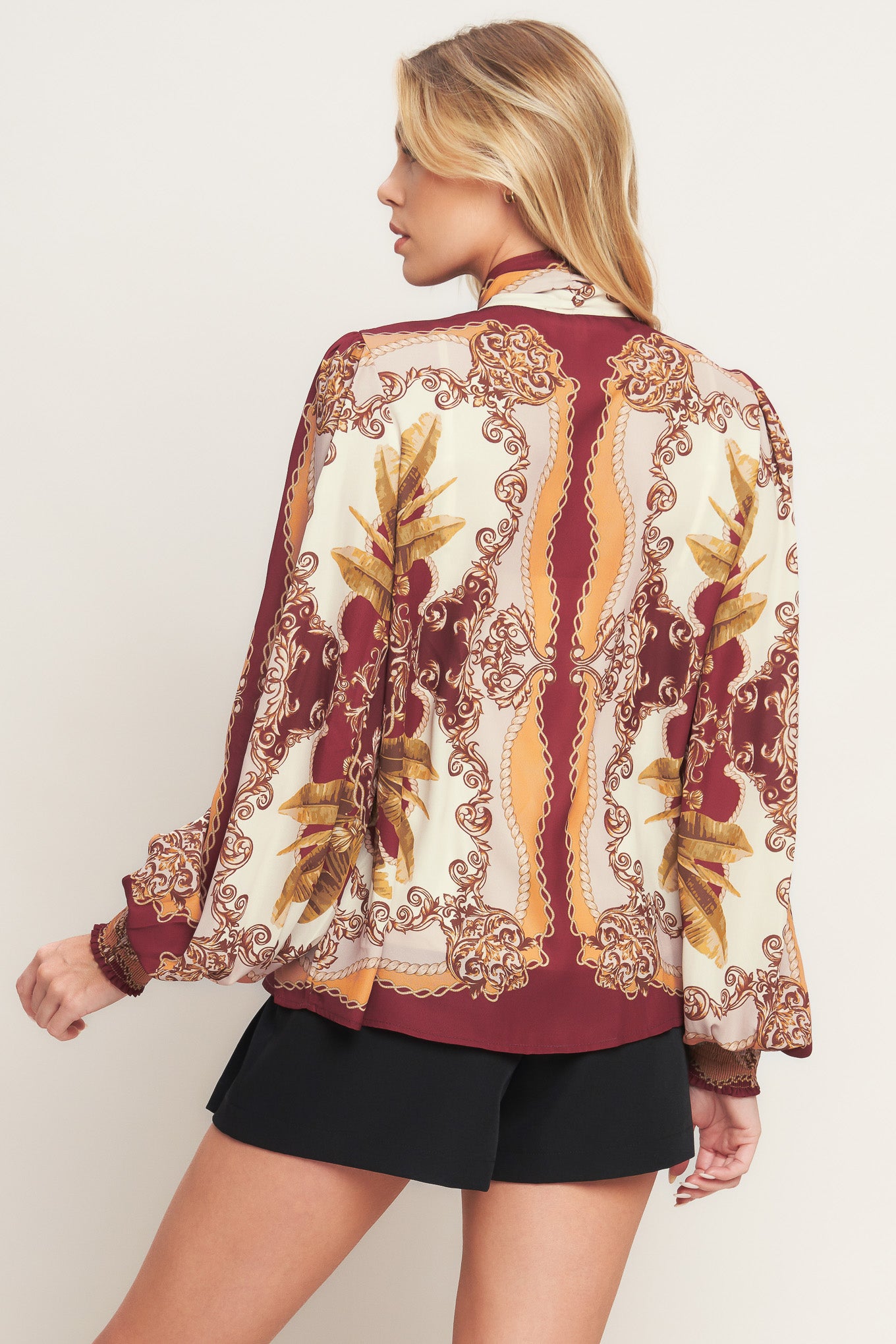 A printed woven top featuring front bow tie, long sleeve with smocked cuff and front button down closure