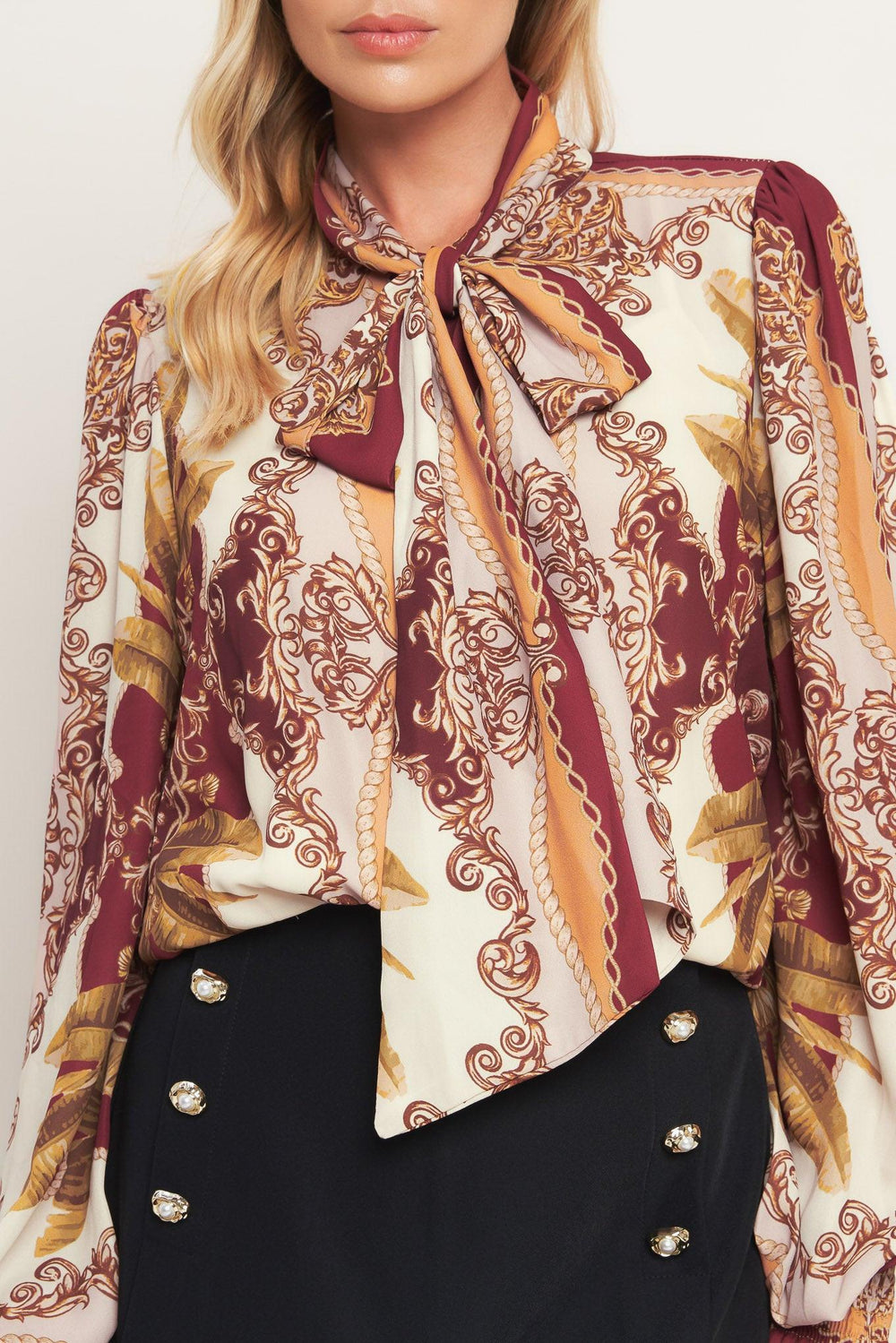 A printed woven top featuring front bow tie, long sleeve with smocked cuff and front button down closure