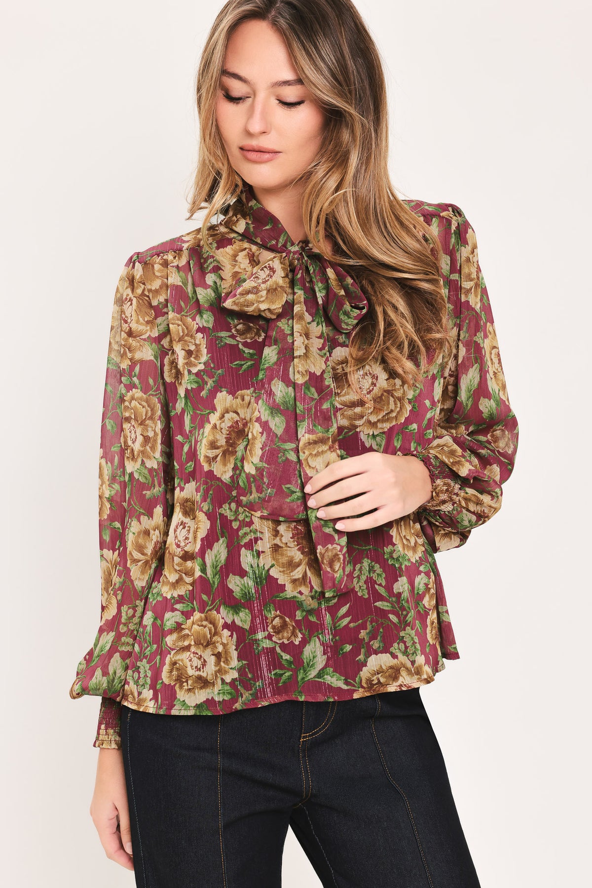 Woman wearing a long sleeve burgundy blouse with floral print and bow tie around the neck | Flying Tomato
