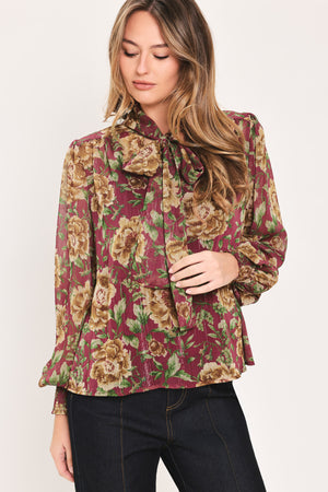 Woman wearing a long sleeve burgundy blouse with floral print and bow tie around the neck | Flying Tomato