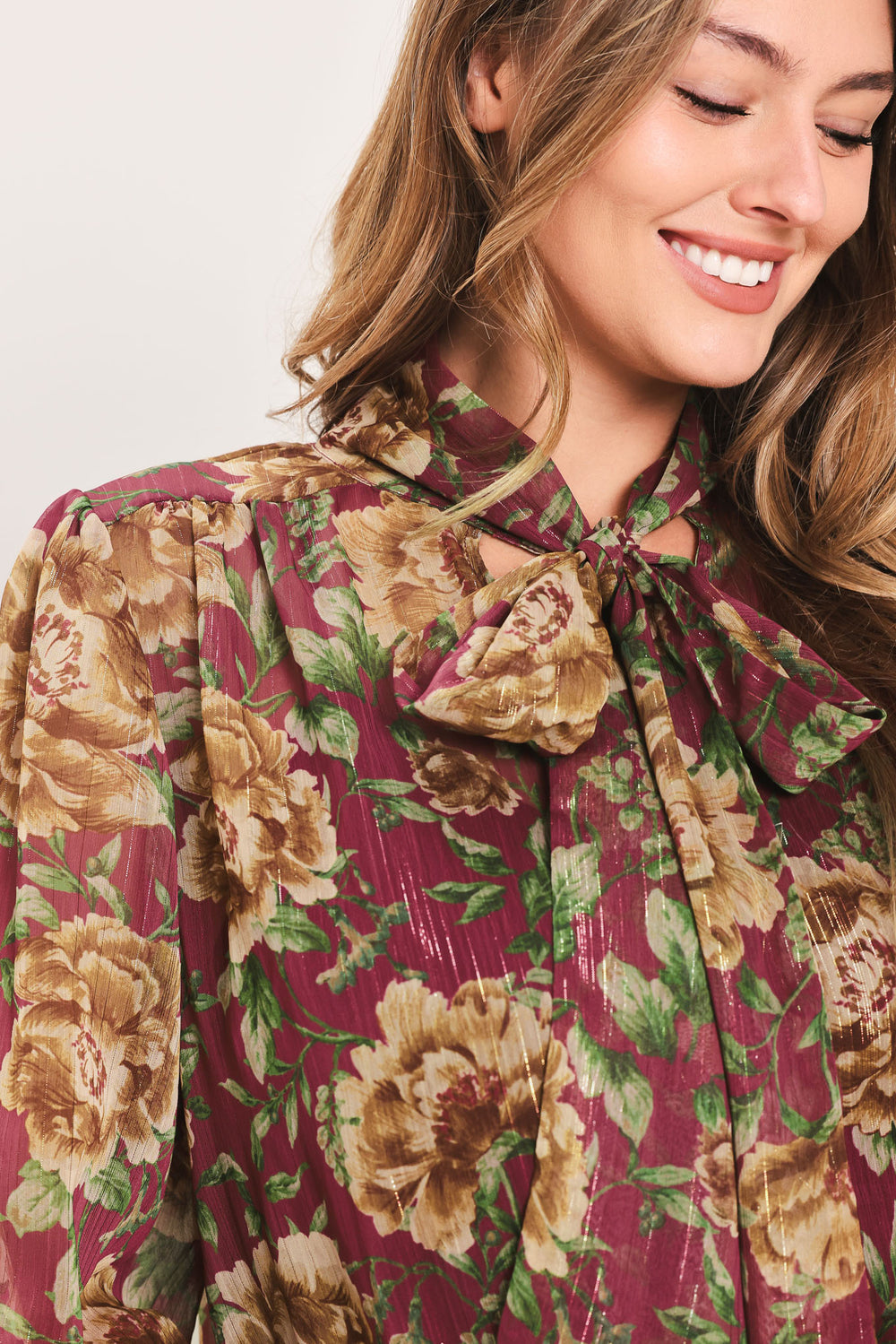 Woman wearing a long sleeve burgundy blouse with floral print and bow tie around the neck | Flying Tomato