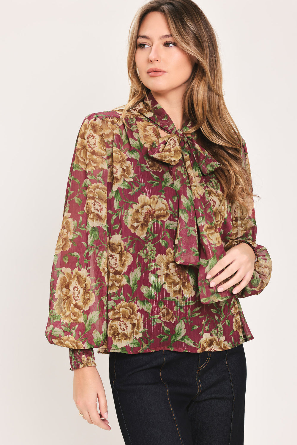 Woman wearing a long sleeve burgundy blouse with floral print and bow tie around the neck | Flying Tomato