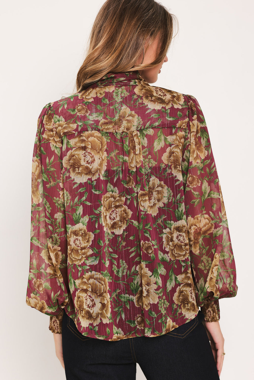 Woman wearing a long sleeve burgundy blouse with floral print and bow tie around the neck | Flying Tomato