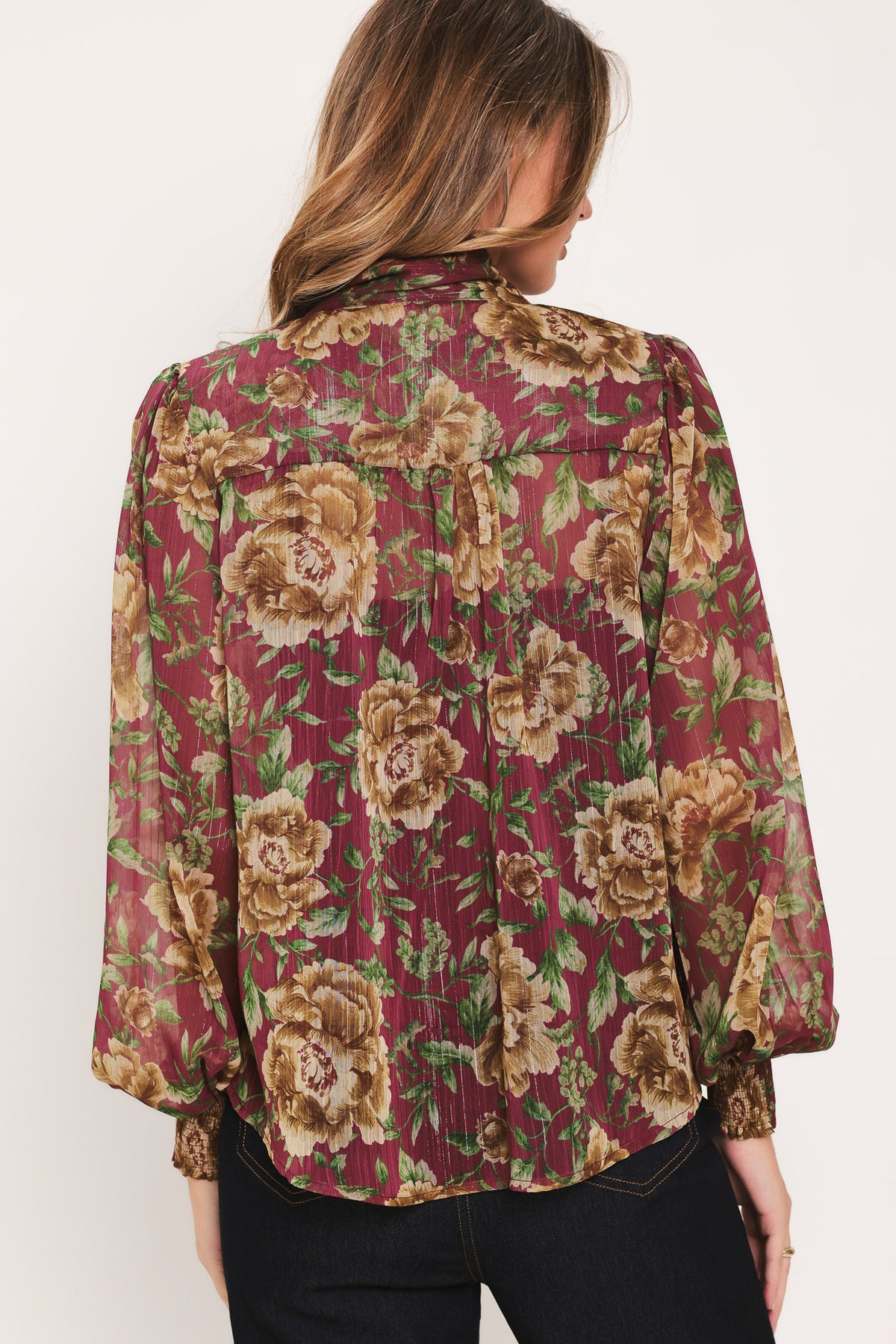 Woman wearing a long sleeve burgundy blouse with floral print and bow tie around the neck | Flying Tomato