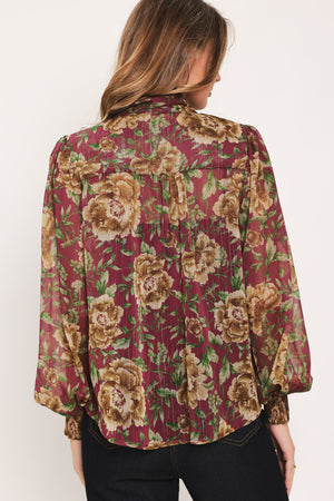 Woman wearing a long sleeve burgundy blouse with floral print and bow tie around the neck | Flying Tomato