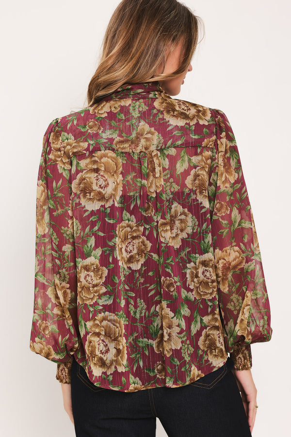 Woman wearing a long sleeve burgundy blouse with floral print and bow tie around the neck | Flying Tomato