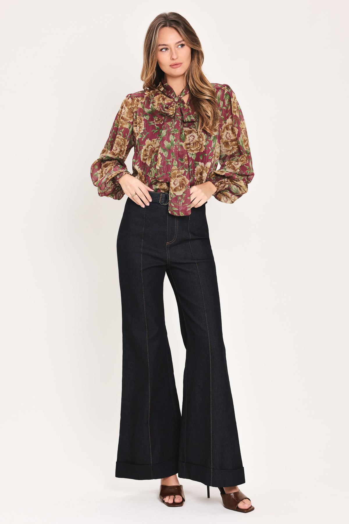 Woman wearing a long sleeve burgundy blouse with floral print and bow tie around the neck | Flying Tomato