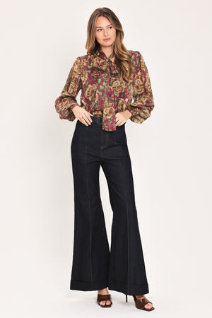 Woman wearing a long sleeve burgundy blouse with floral print and bow tie around the neck | Flying Tomato