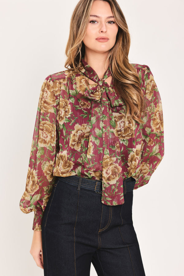 Woman wearing a long sleeve burgundy blouse with floral print and bow tie around the neck | Flying Tomato
