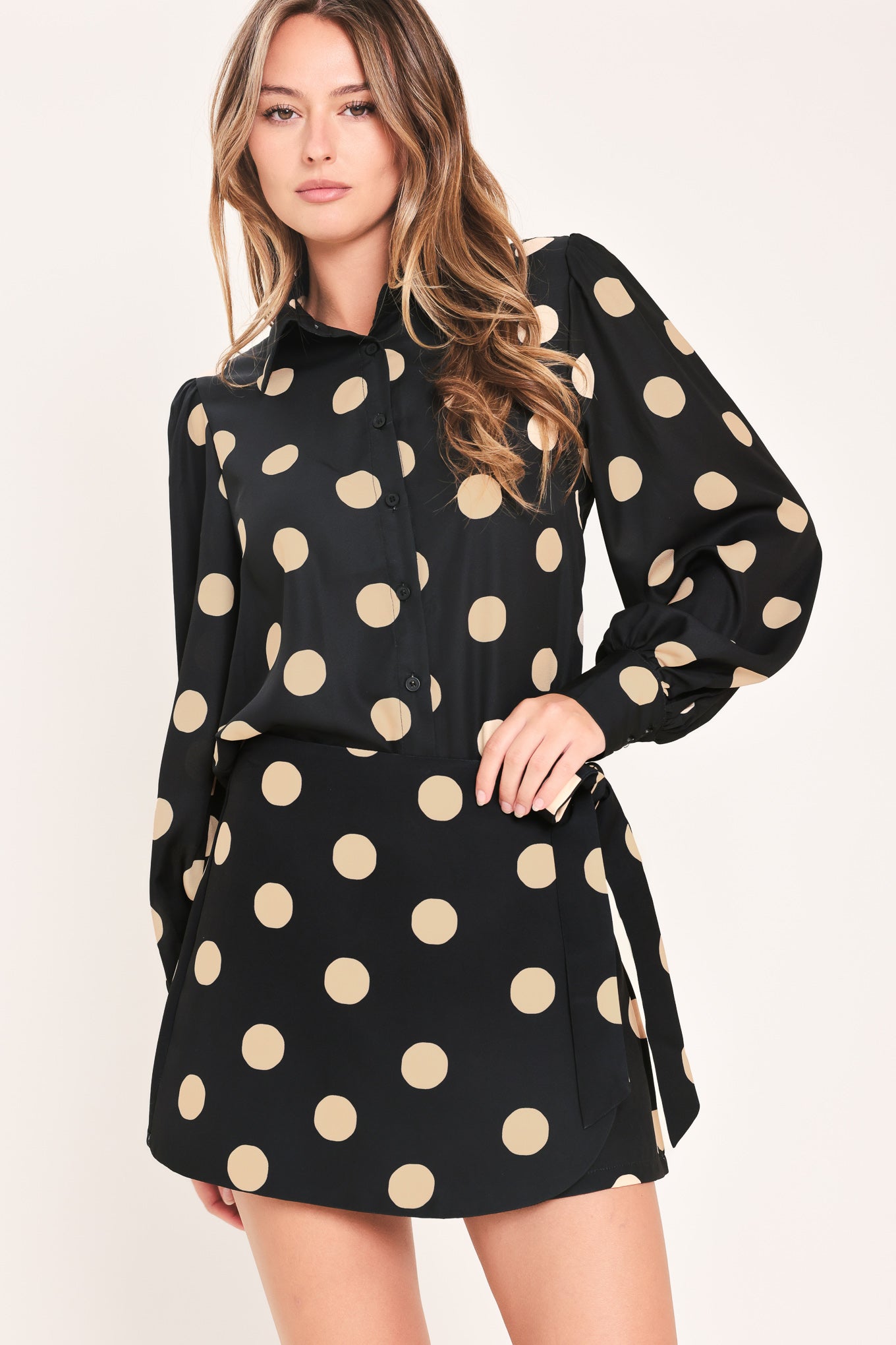 A woman wearing a polka dot printed woven top featuring collar, long sleeve with button down closure | Flying Tomato