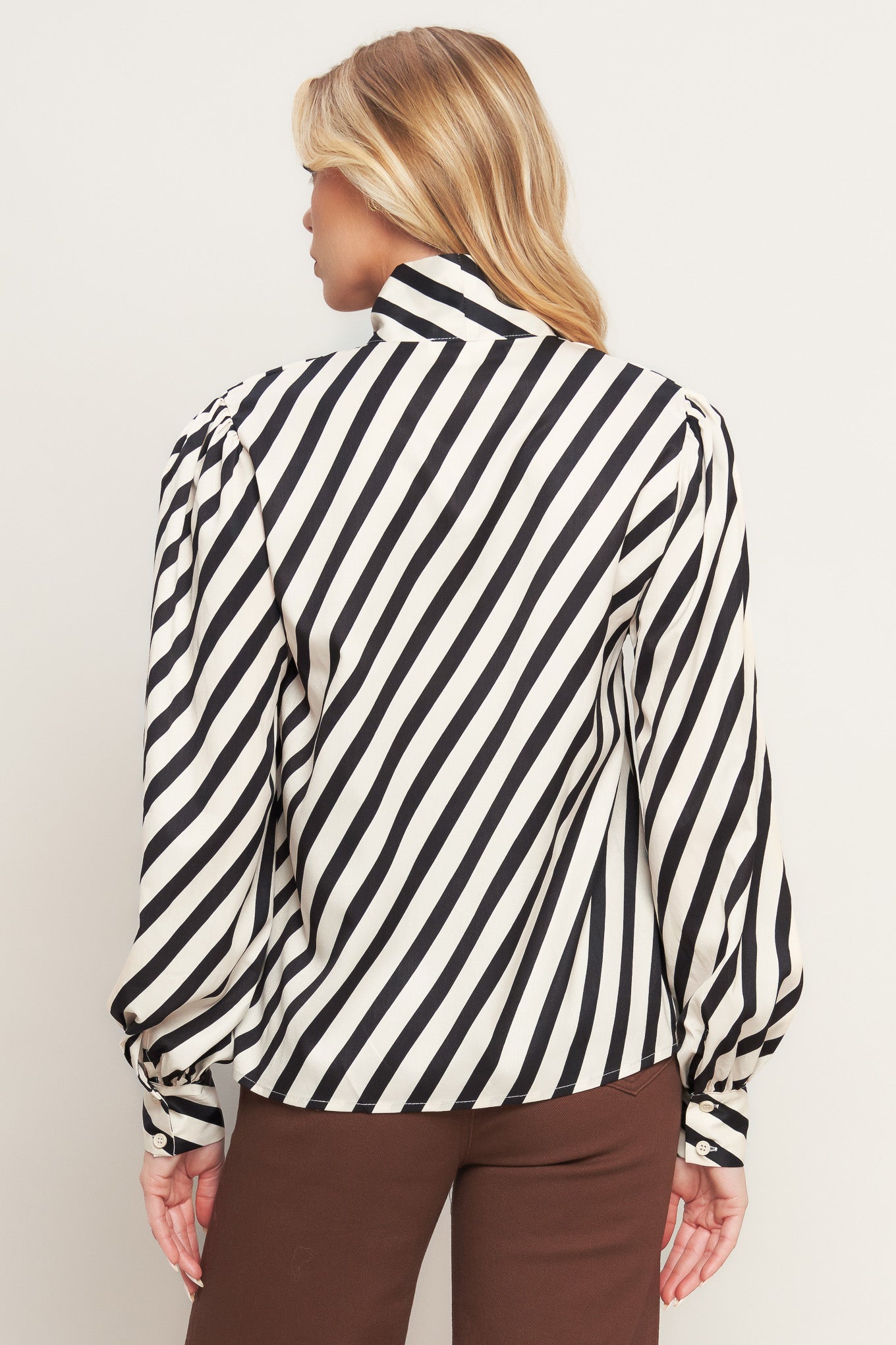 A striped woven top featuring high neckline with front bow tie and long sleeve with cuff