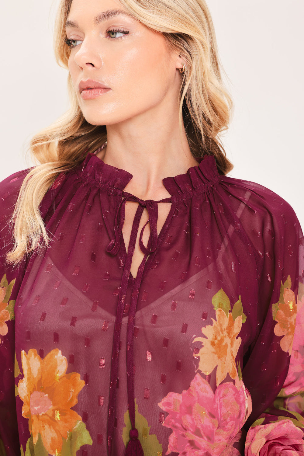 A woman wearing a sheer long-sleeve blouse with a floral print in pink, yellow, and green over a deep burgundy base | Flying Tomato