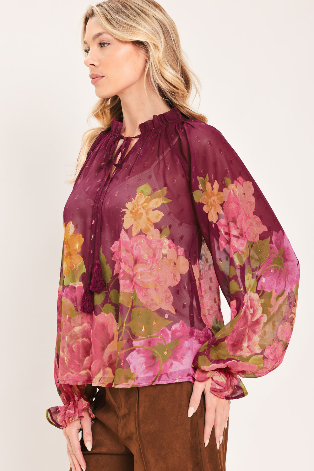 A woman wearing a sheer long-sleeve blouse with a floral print in pink, yellow, and green over a deep burgundy base | Flying Tomato