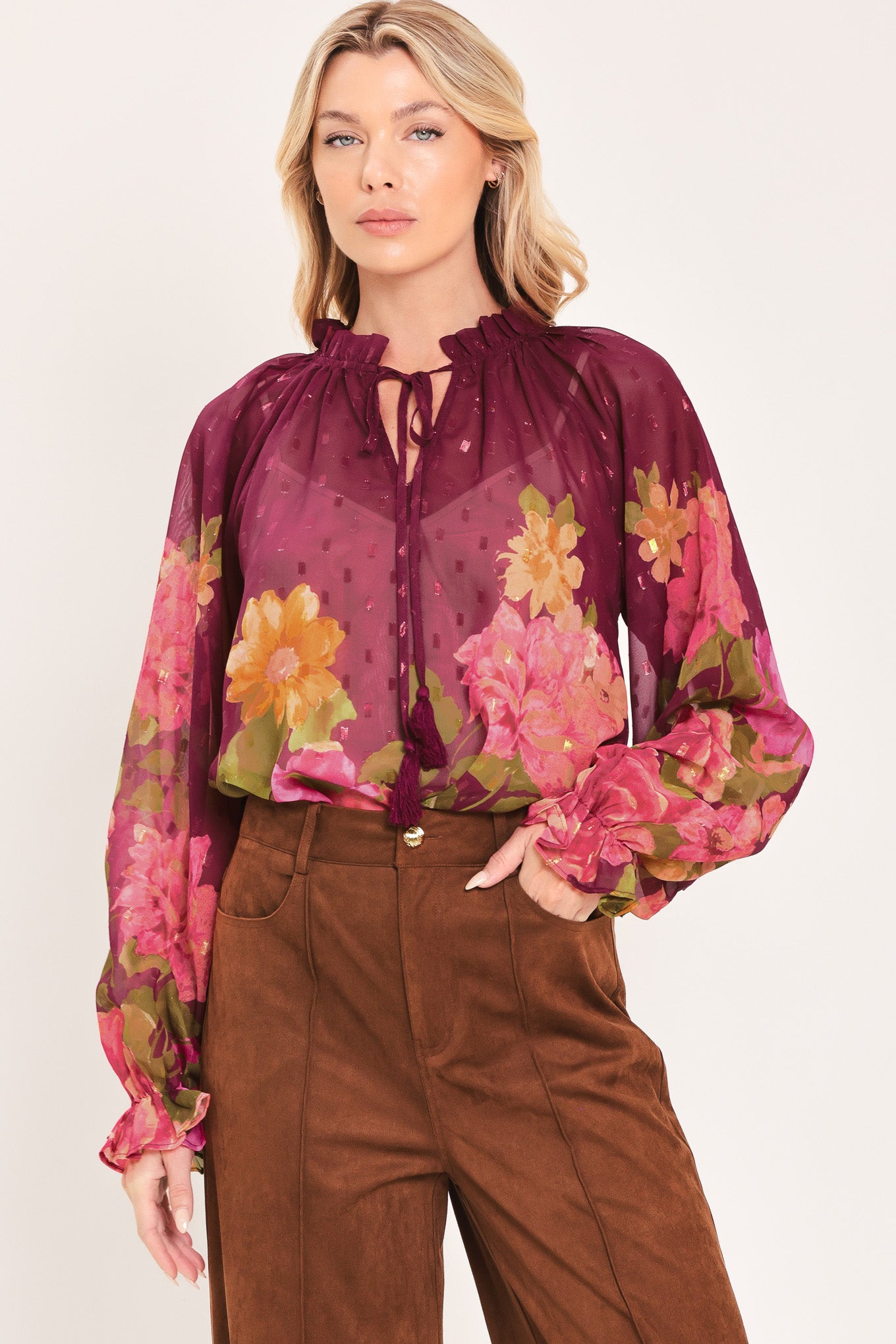A woman wearing a sheer long-sleeve blouse with a floral print in pink, yellow, and green over a deep burgundy base | Flying Tomato