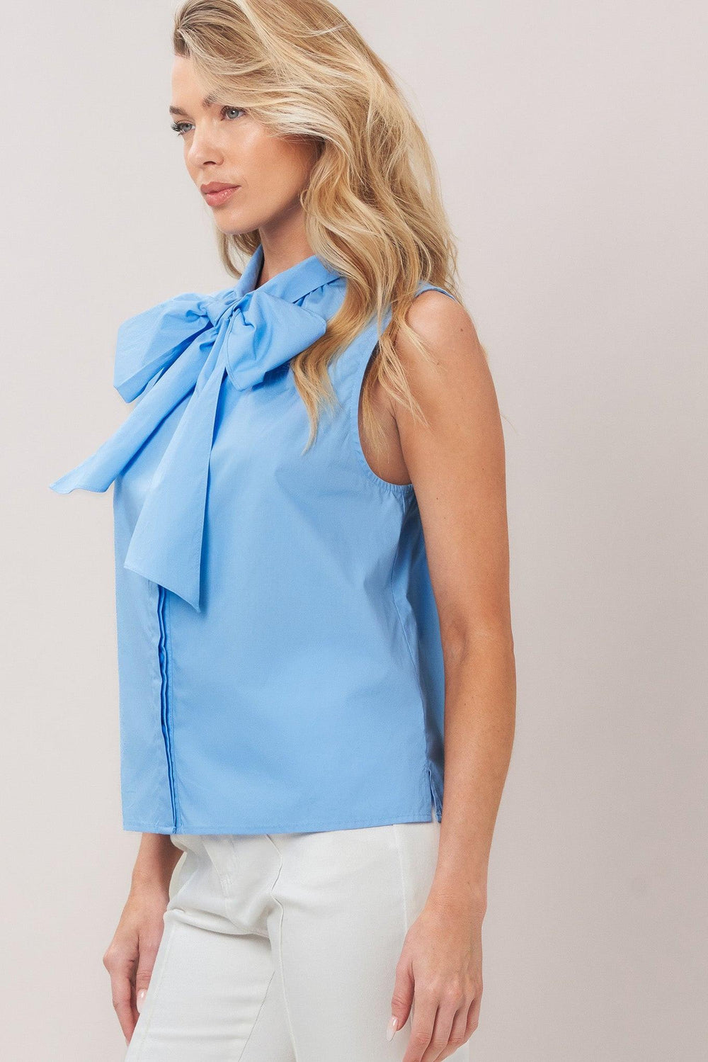 Woman wearing a light blue sleeveless top with a large bow detail on a plain background
