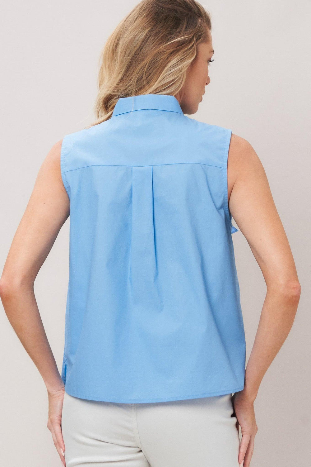 Woman wearing a light blue sleeveless top with a large bow detail on a plain background