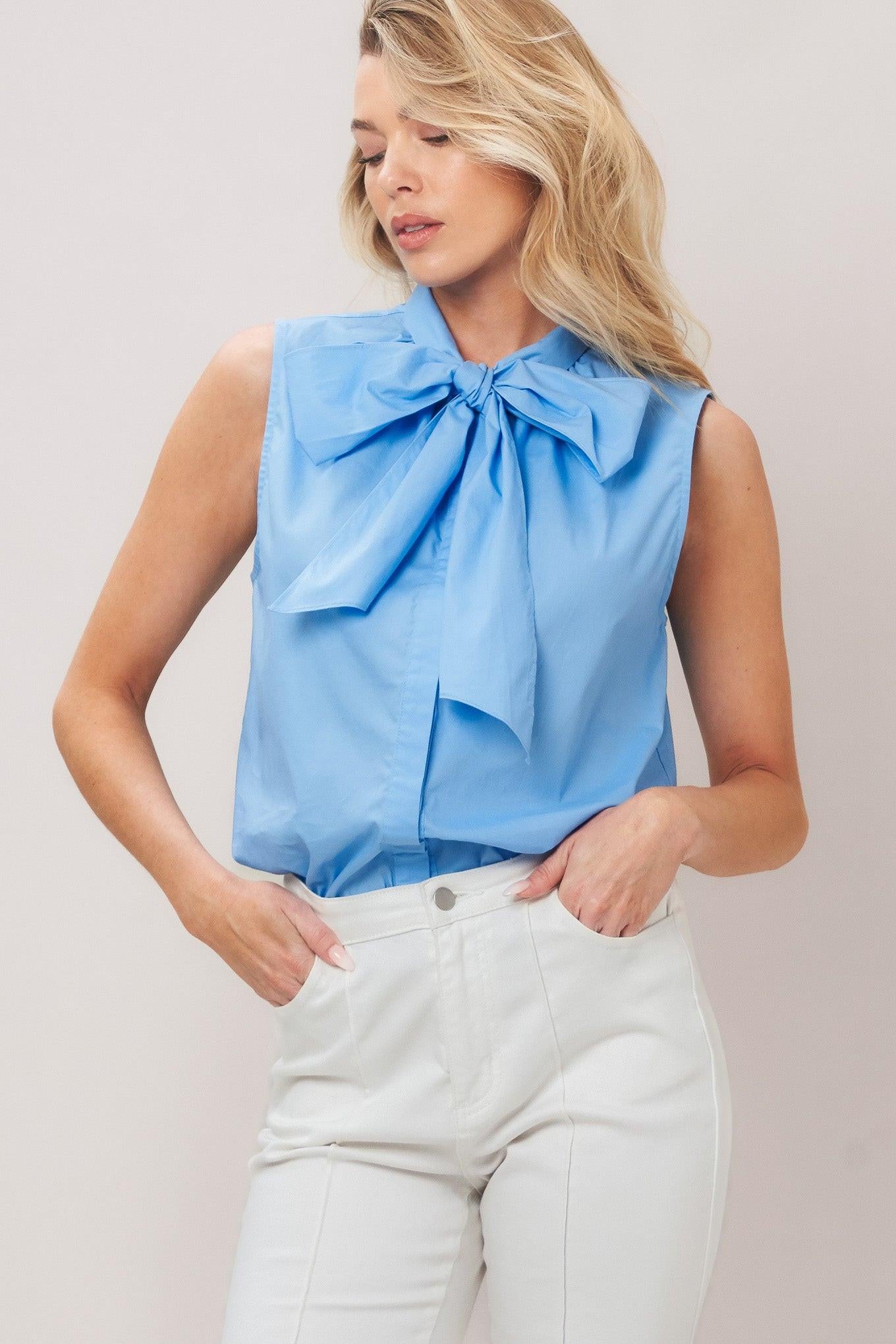 Woman wearing a light blue sleeveless top with a bow detail against a plain background