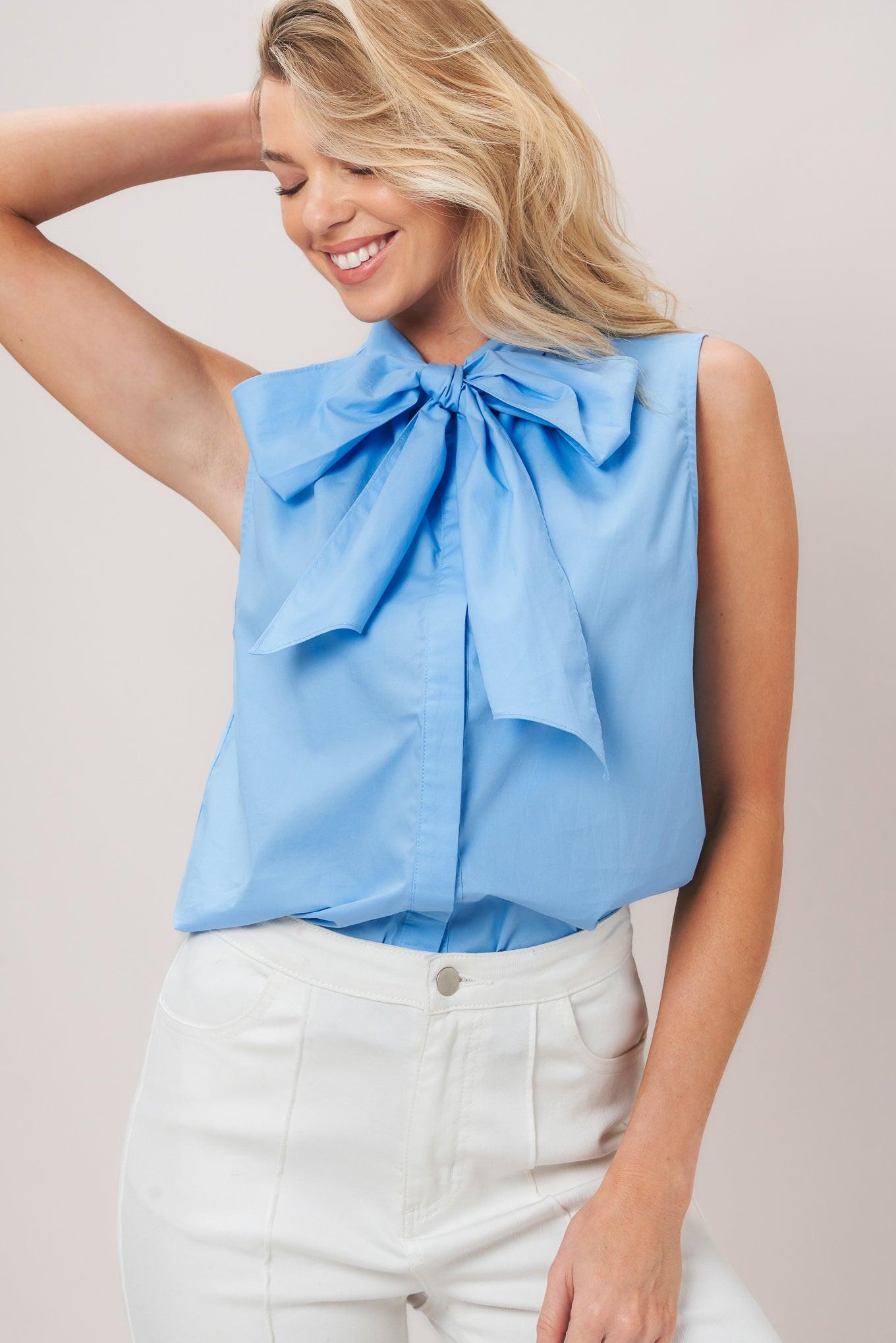 Woman wearing a light blue sleeveless top with a large bow detail on a plain background
