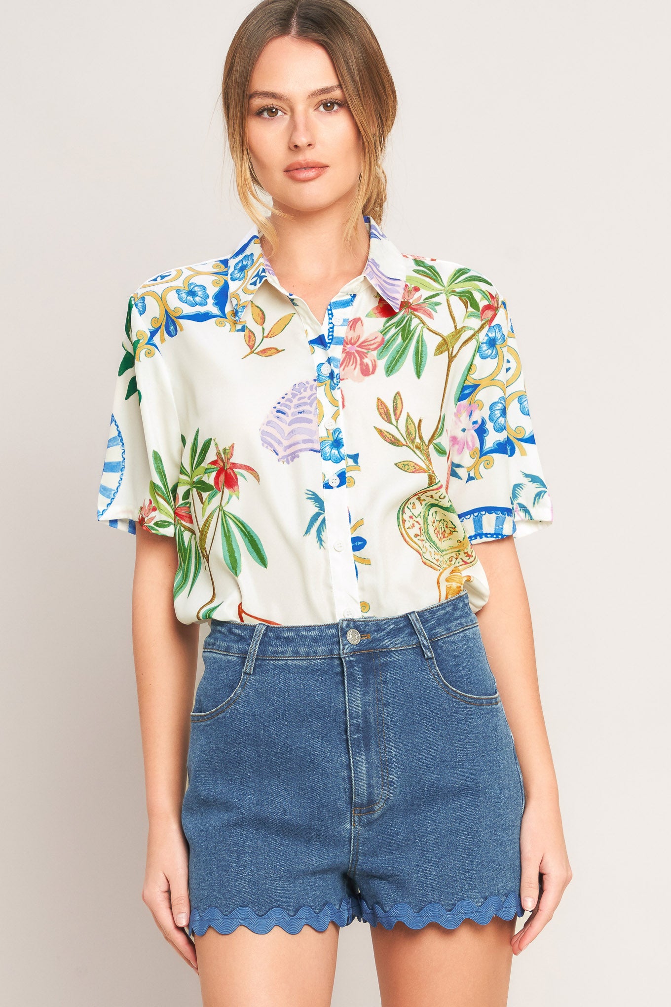 Woman wearing a colorful floral shirt and denim shorts on a plain background