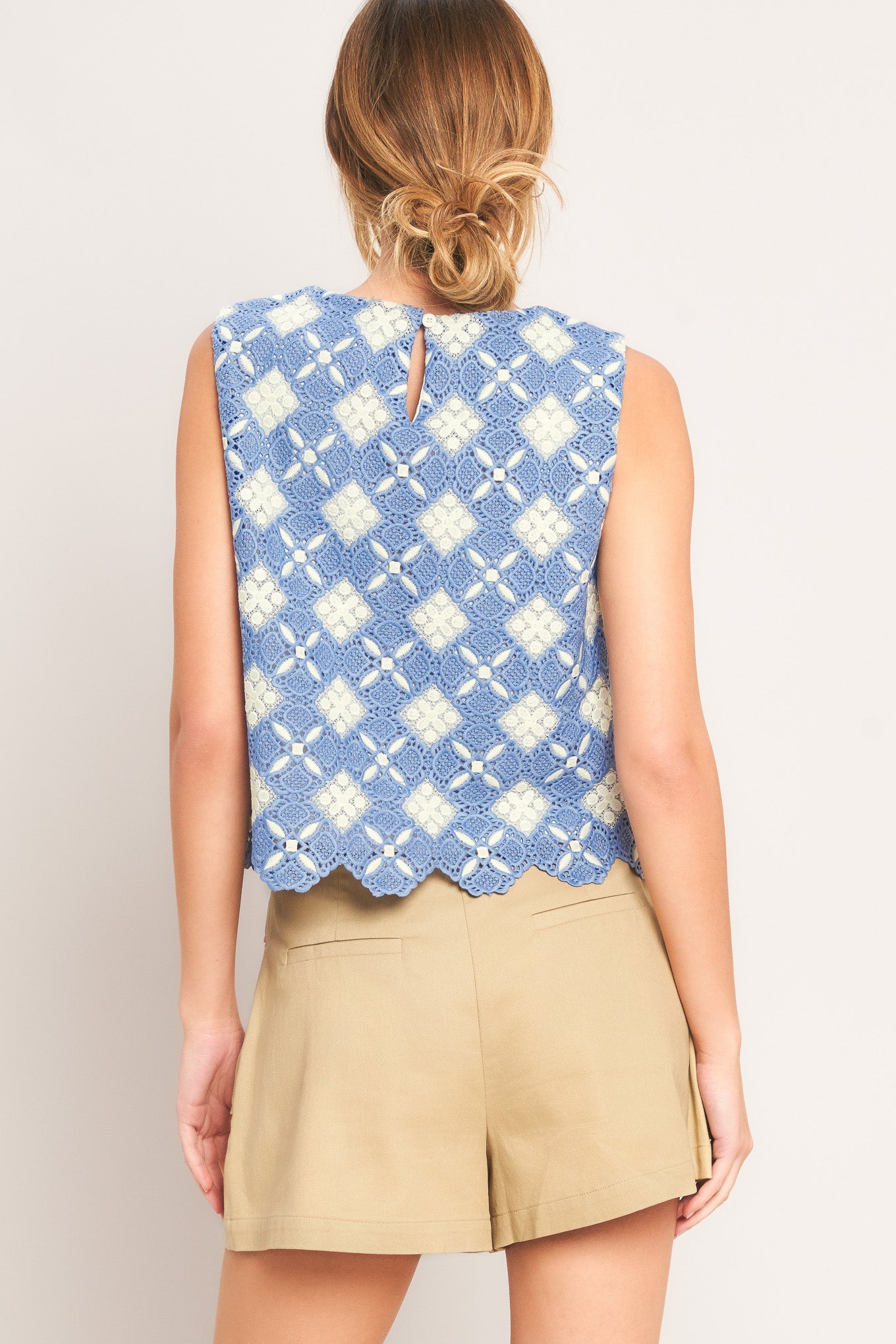 Woman wearing a sleeveless blue and white patterned top with beige shorts on a plain background