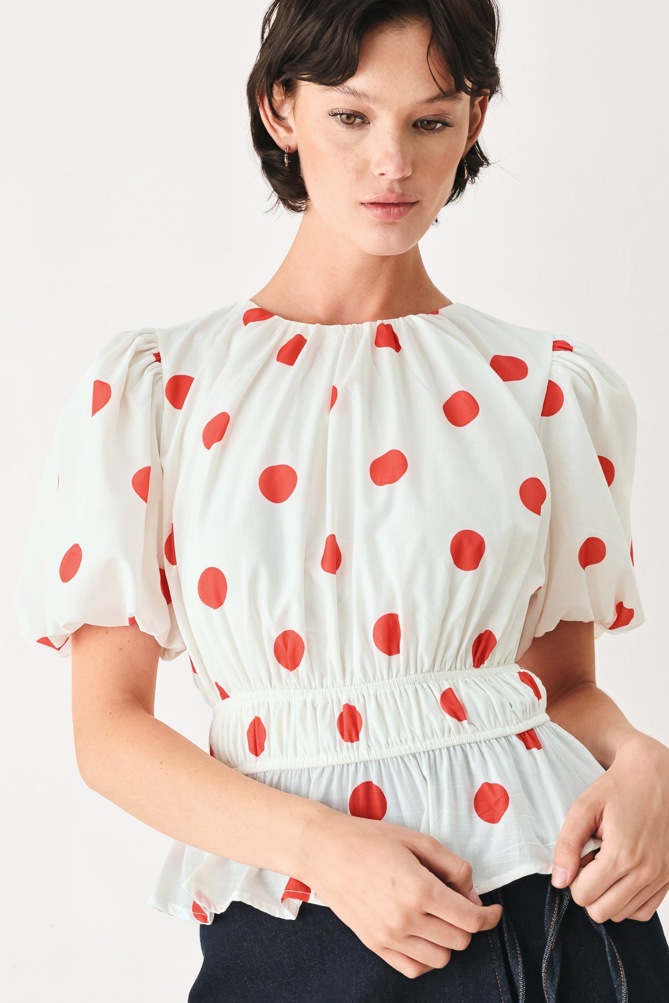 Woman wearing a white blouse with red polka dots featuring round neckline, short bubble sleeve, double elastic waist and back neck button closure | FREEMARKET