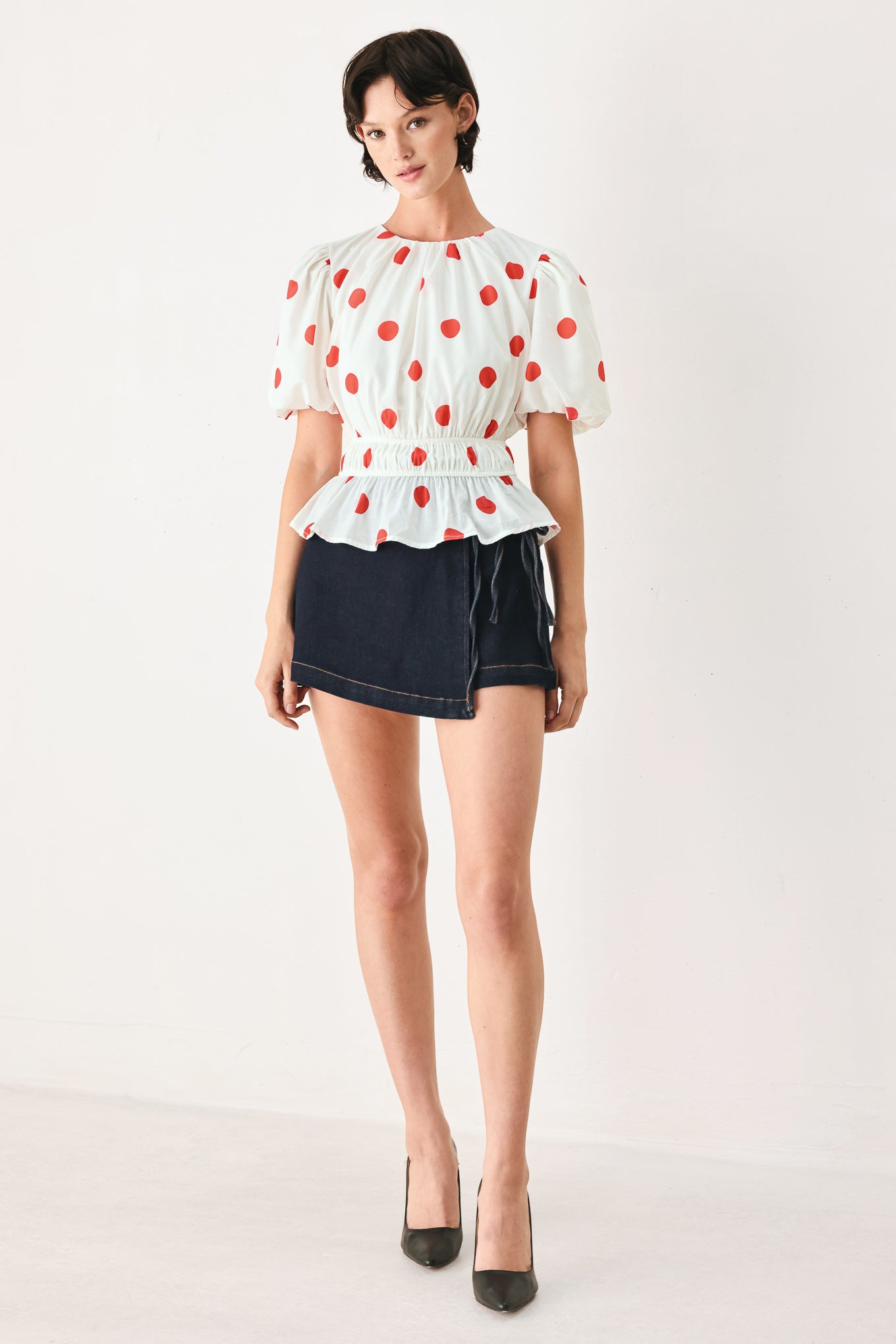 Woman wearing a white blouse with red polka dots featuring round neckline, short bubble sleeve, double elastic waist and back neck button closure | FREEMARKET