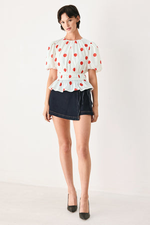 Woman wearing a white blouse with red polka dots featuring round neckline, short bubble sleeve, double elastic waist and back neck button closure | FREEMARKET