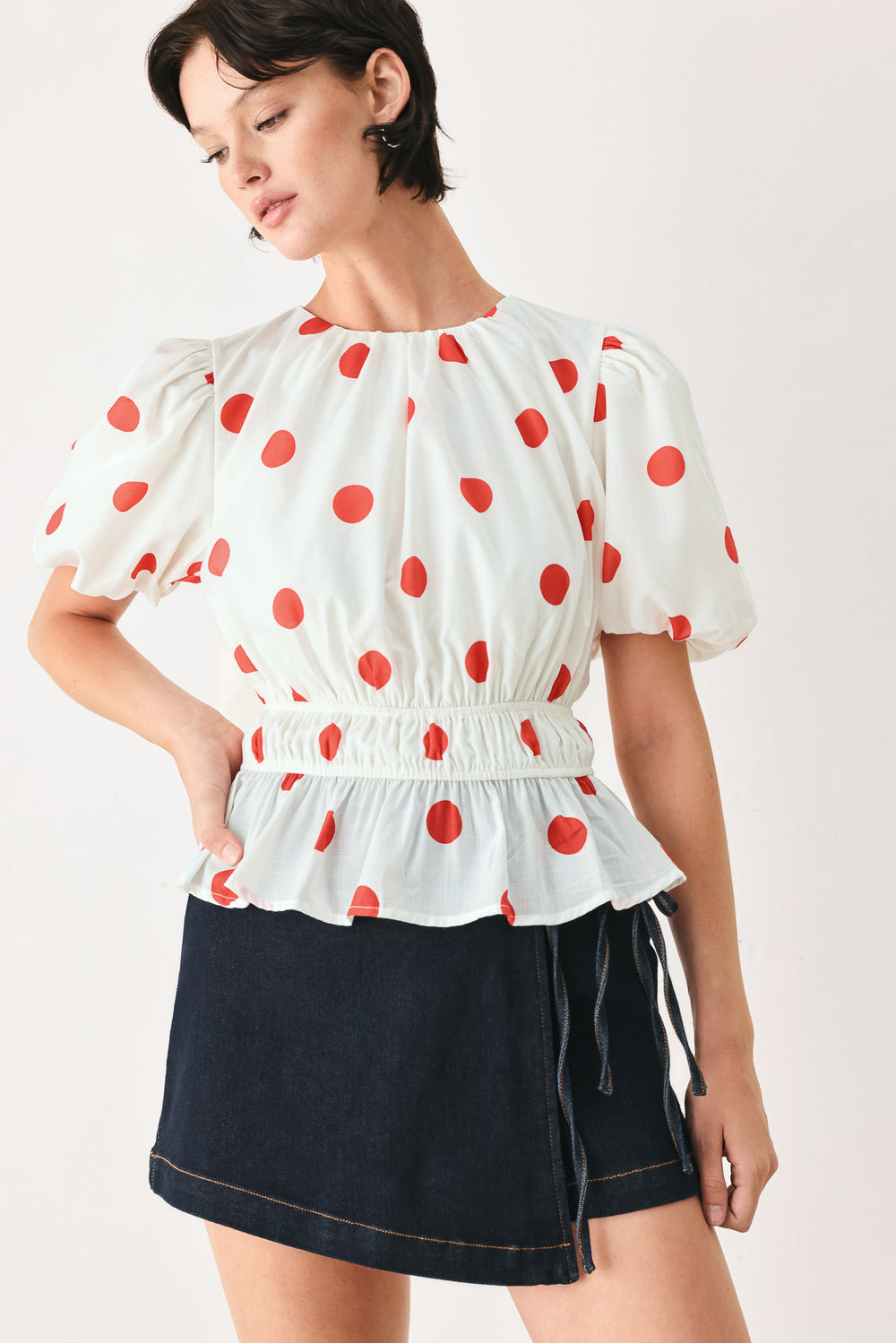 Woman wearing a white blouse with red polka dots featuring round neckline, short bubble sleeve, double elastic waist and back neck button closure | FREEMARKET