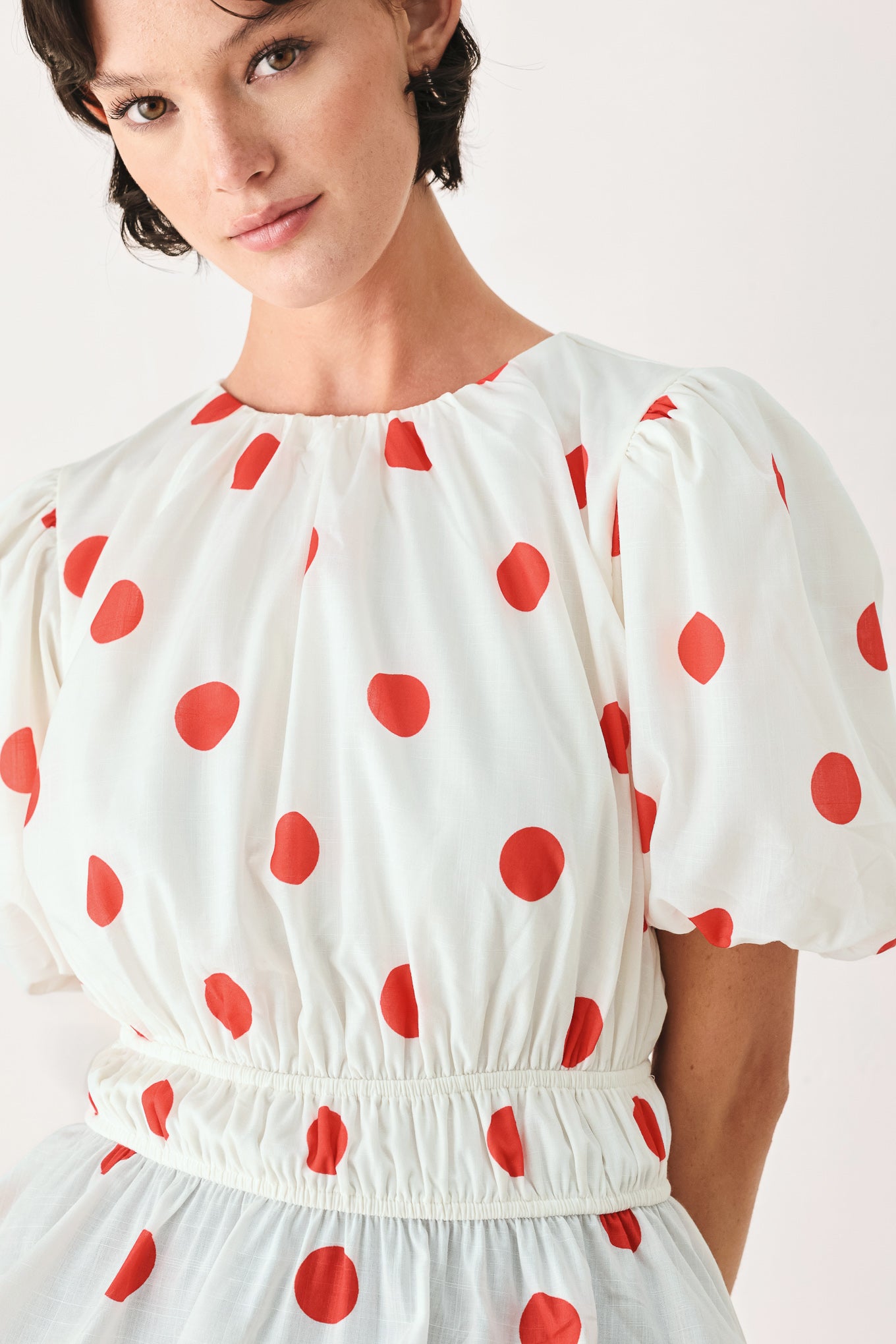 Woman wearing a white blouse with red polka dots featuring round neckline, short bubble sleeve, double elastic waist and back neck button closure | FREEMARKET
