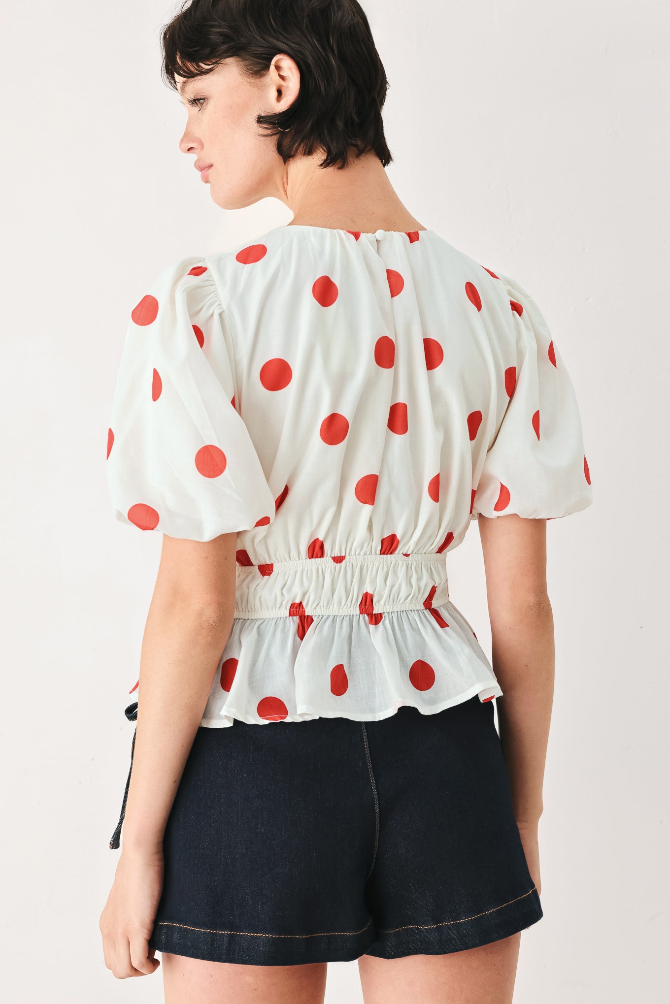 Woman wearing a white blouse with red polka dots featuring round neckline, short bubble sleeve, double elastic waist and back neck button closure | FREEMARKET
