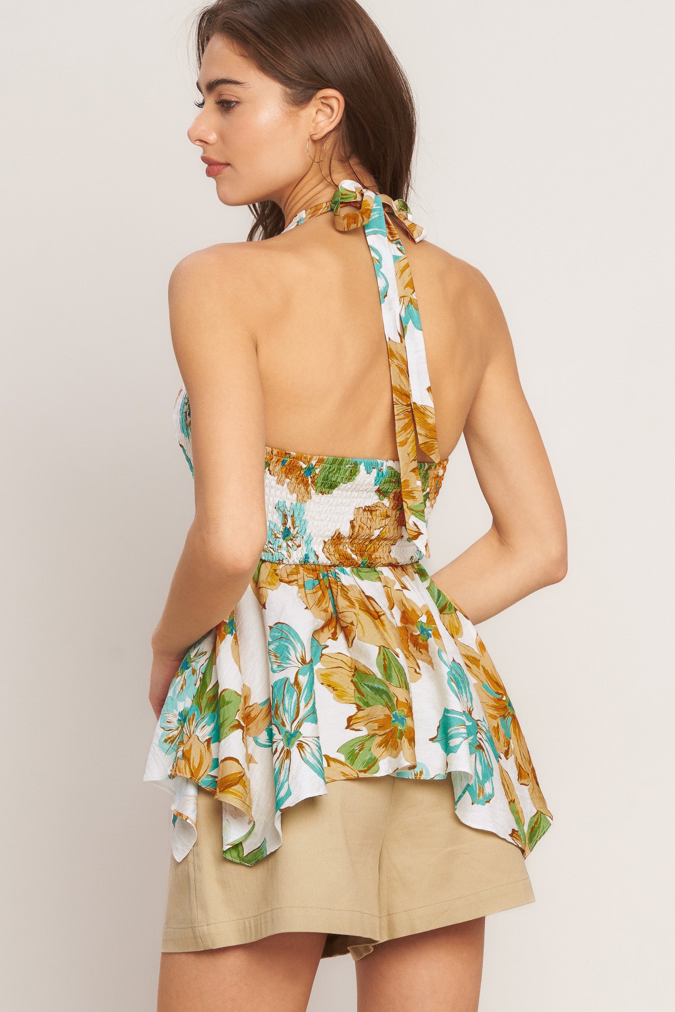 Woman wearing a floral halter top with beige shorts on a plain background