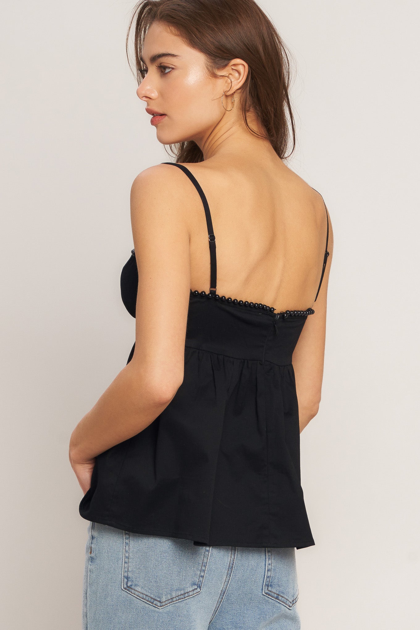 A black solid woven top featuring twisted bodice with bead trim, straps and back zipper closure