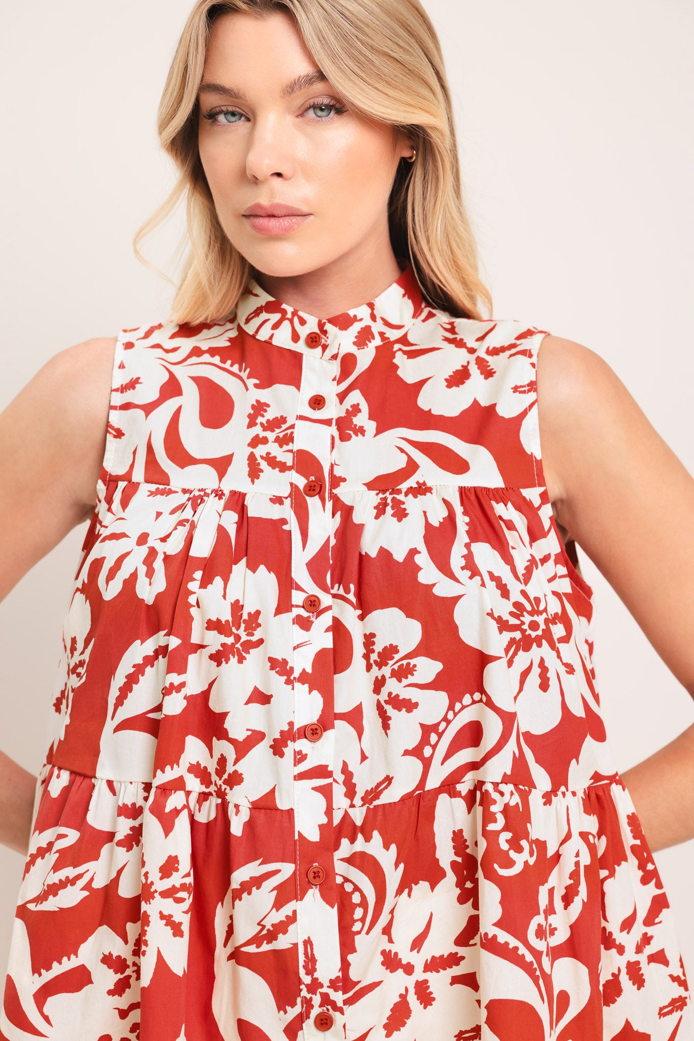 Woman wearing a red and white floral sleeveless top with tiers and front button closure | Flying Tomato