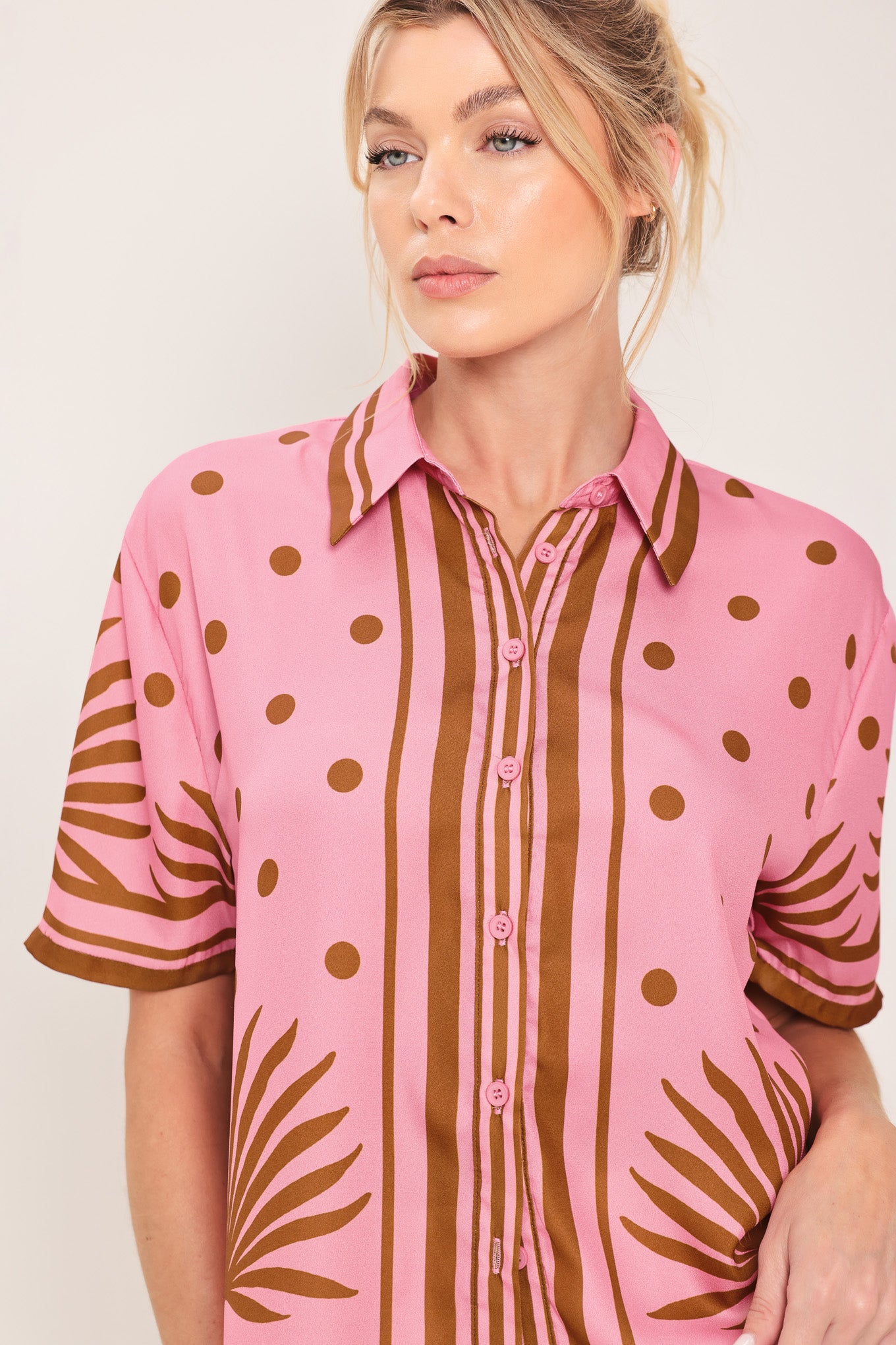 Woman wearing a pink button up top with brown polka dots and printed palms | Flying Tomato