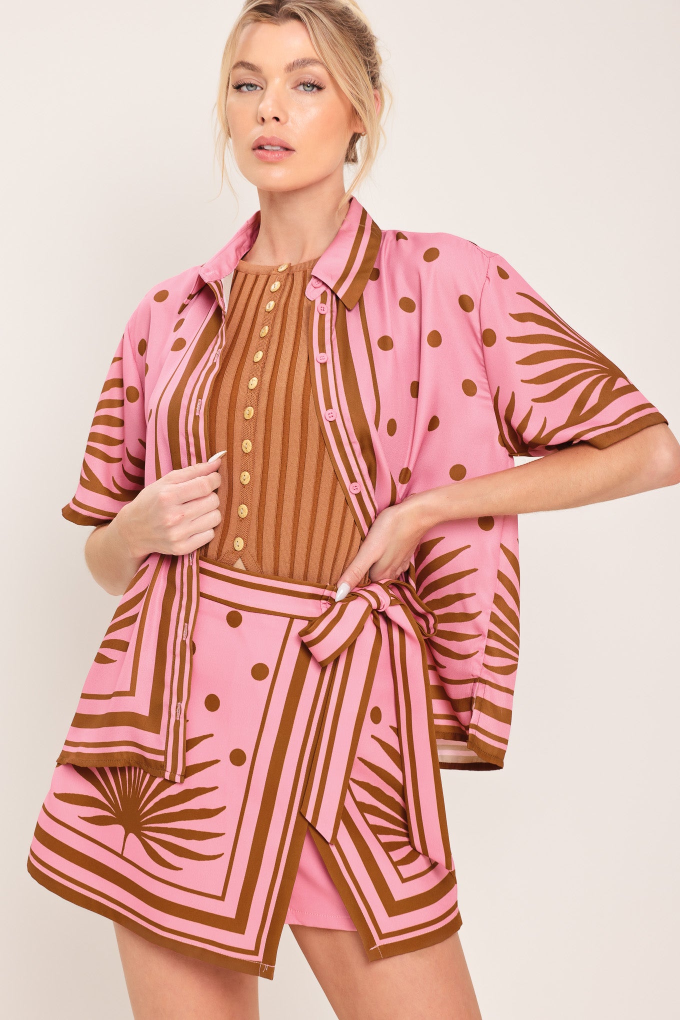Woman wearing a pink button up top with brown polka dots and printed palms | Flying Tomato