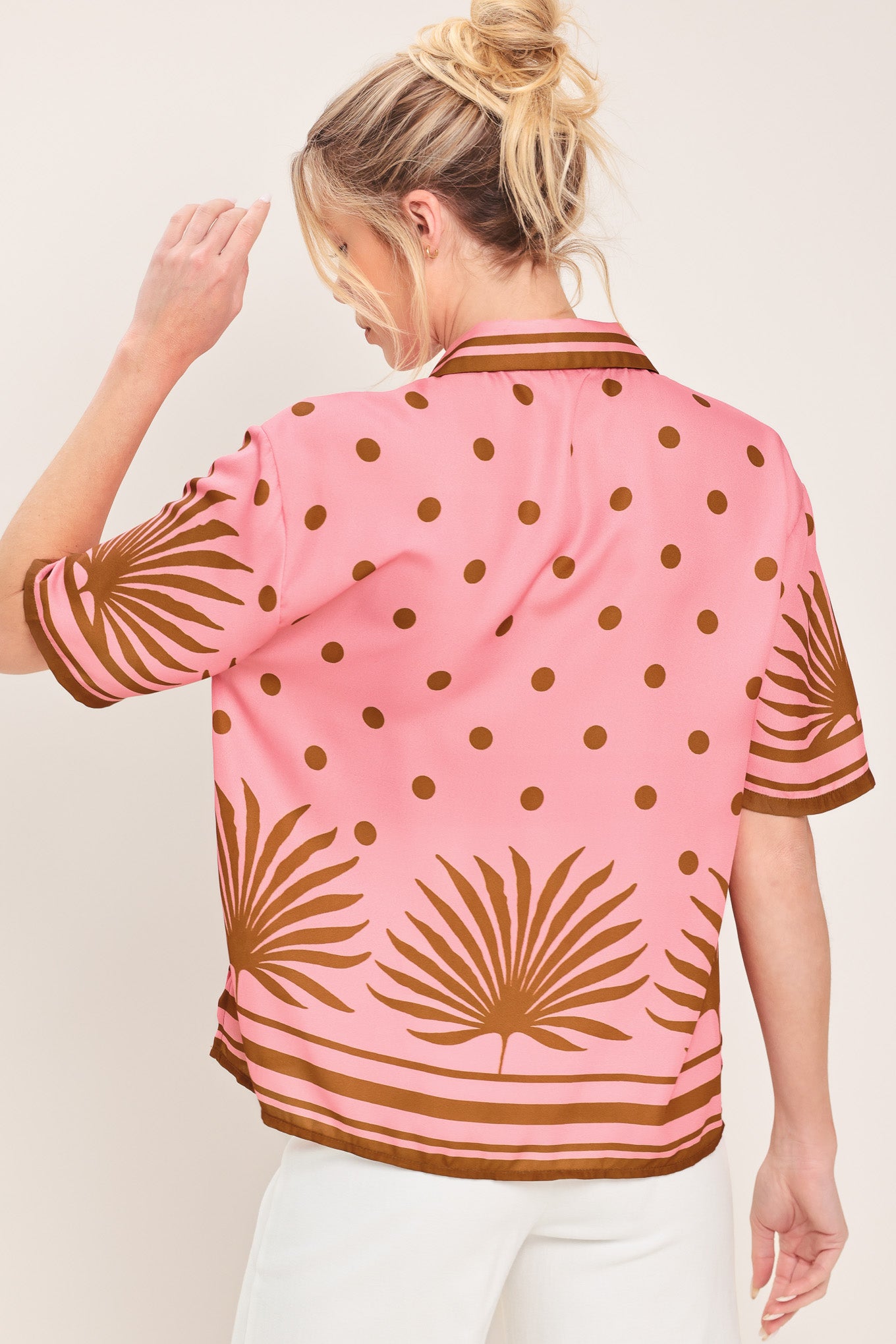 Woman wearing a pink button up top with brown polka dots and printed palms | Flying Tomato