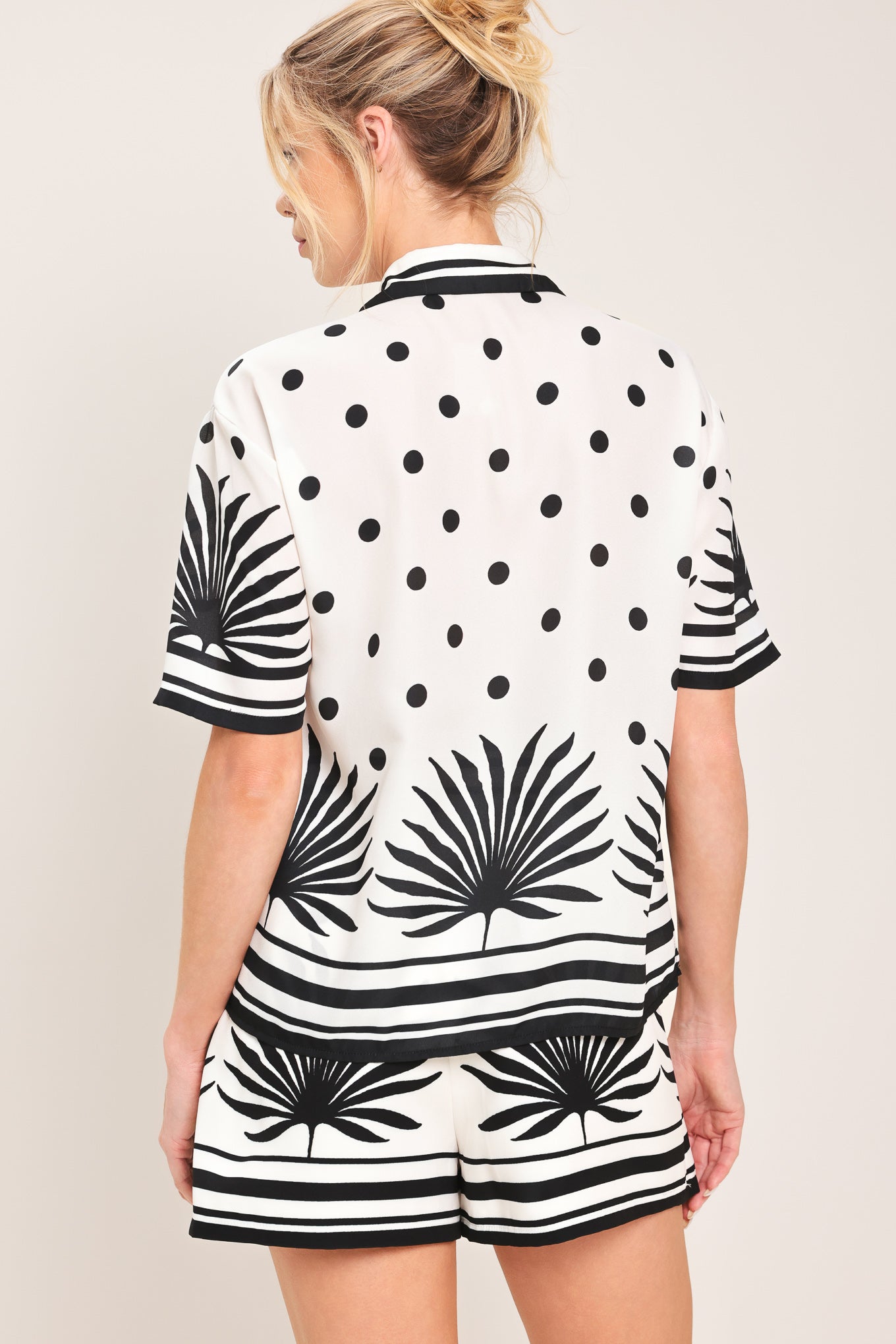 Woman wearing a white button up top with black polka dots and printed palms | Flying Tomato