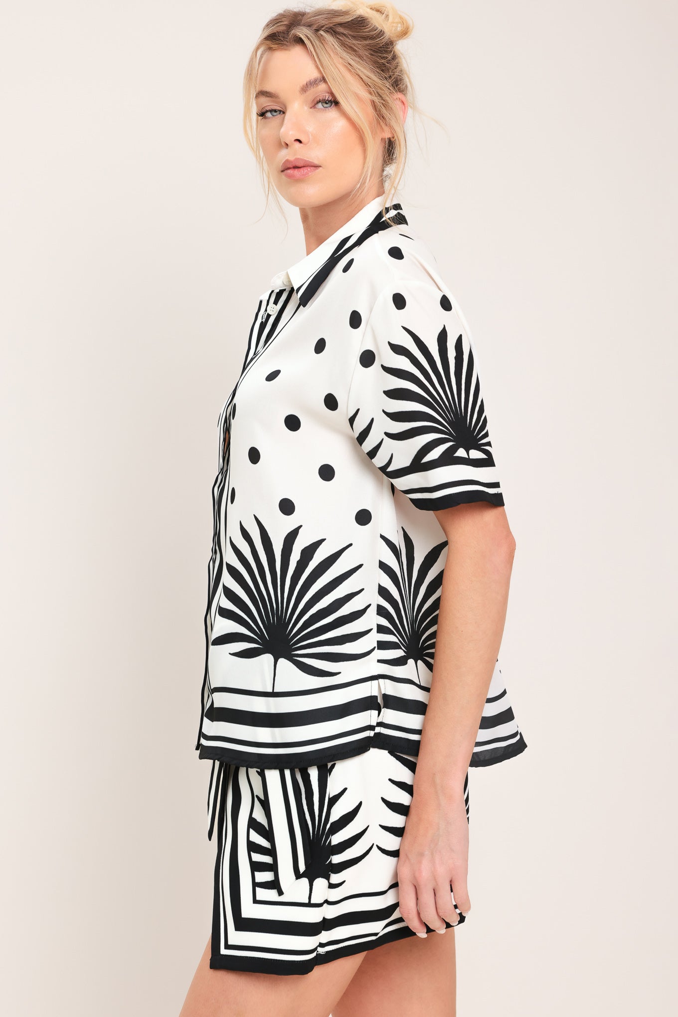 Woman wearing a white button up top with black polka dots and printed palms | Flying Tomato