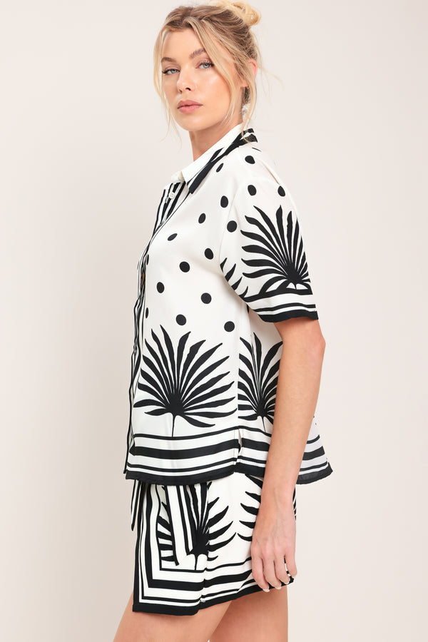 Woman wearing a white button up top with black polka dots and printed palms | Flying Tomato